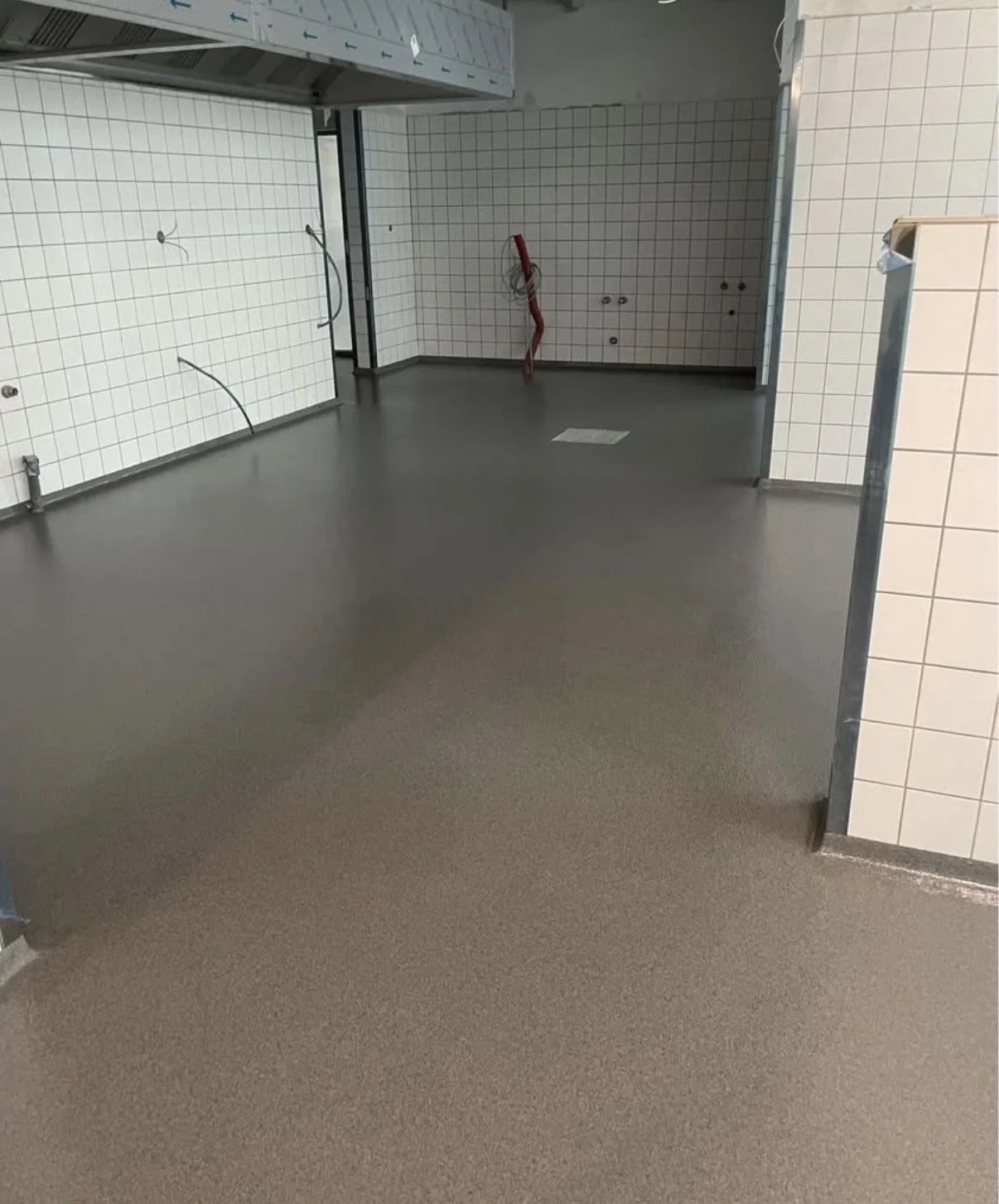 Ufærdig vinksel med hvide tiledæk og tomme vægge, der er elektriske installationer og et afløb i gulvet.