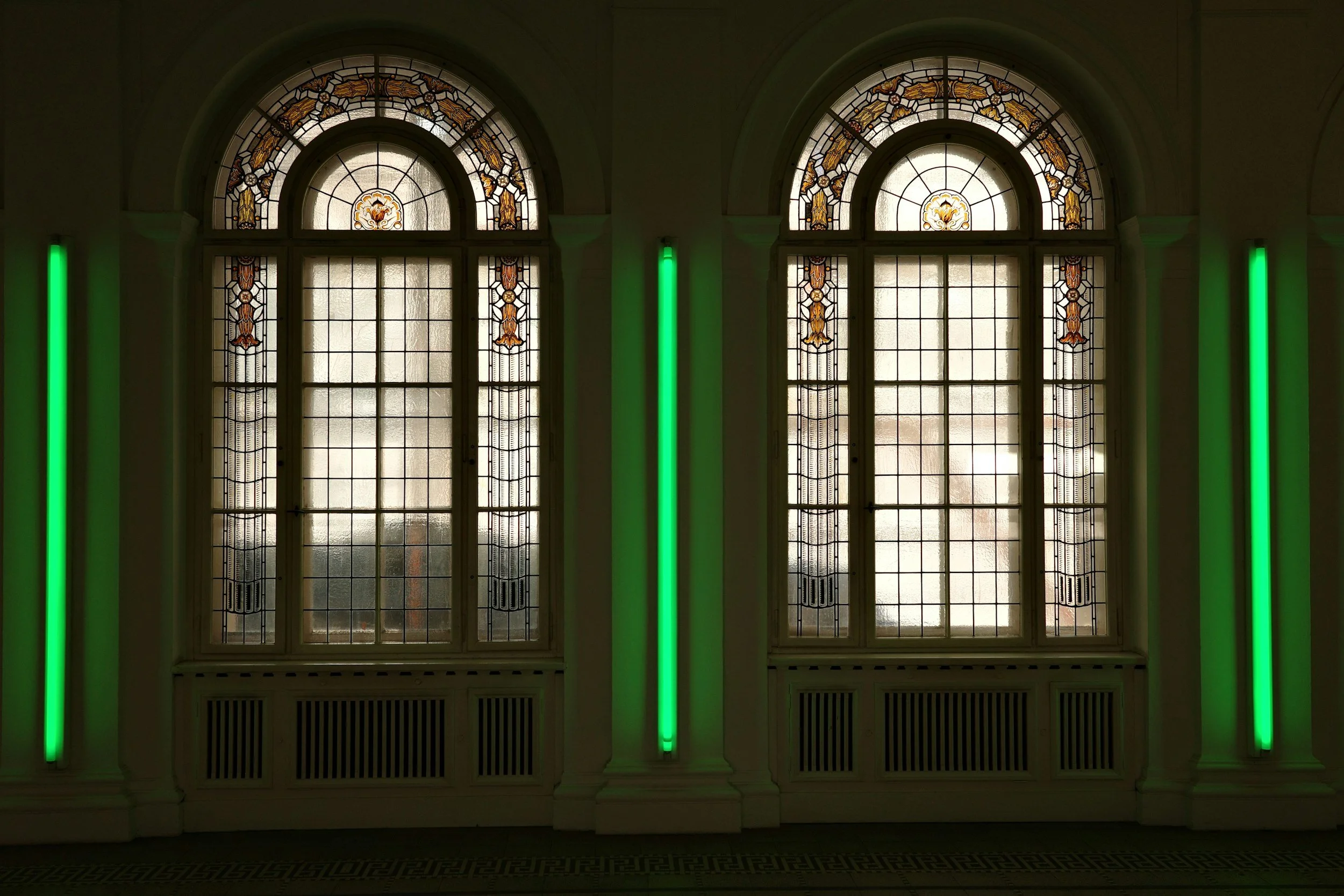 Interior view of a historic building with large stained glass windows and green neon lights on the walls.