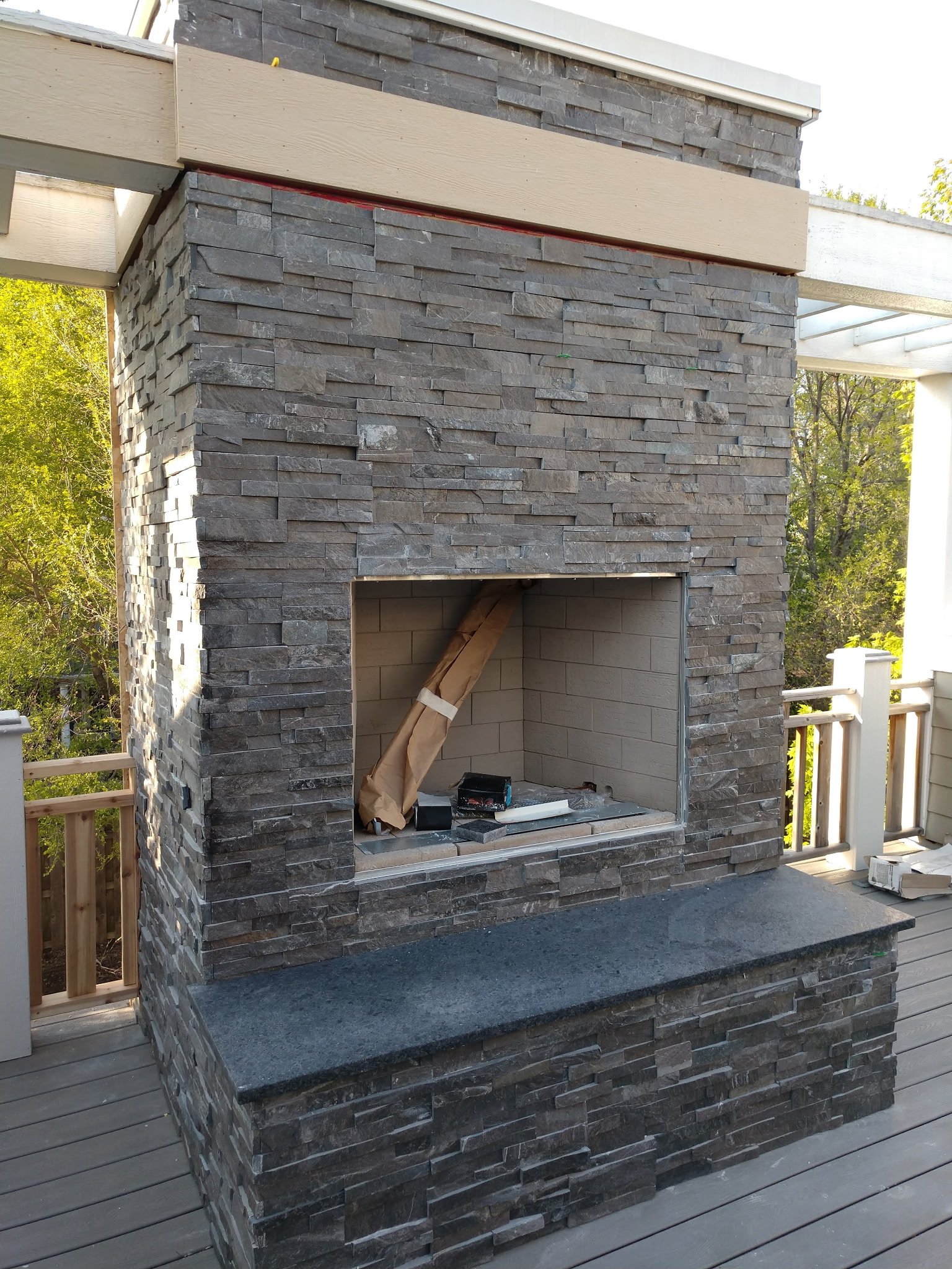An outdoor fireplace under construction, with a dark stone exterior, a granite hearth, and unfinished interior space.