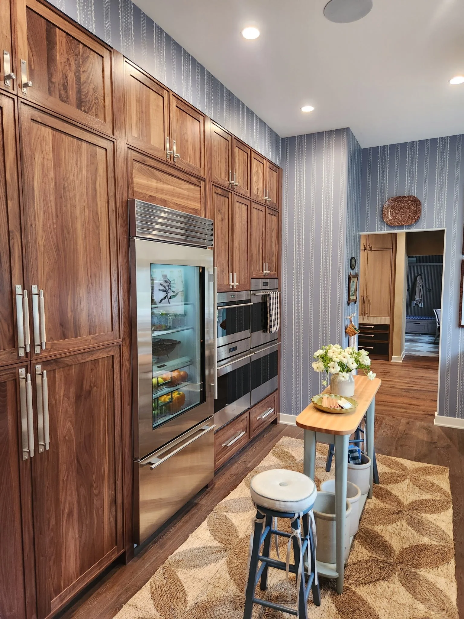 A kitchen with wooden cabinets, stainless steel appliances, a small table with flowers, and a rug on the floor.