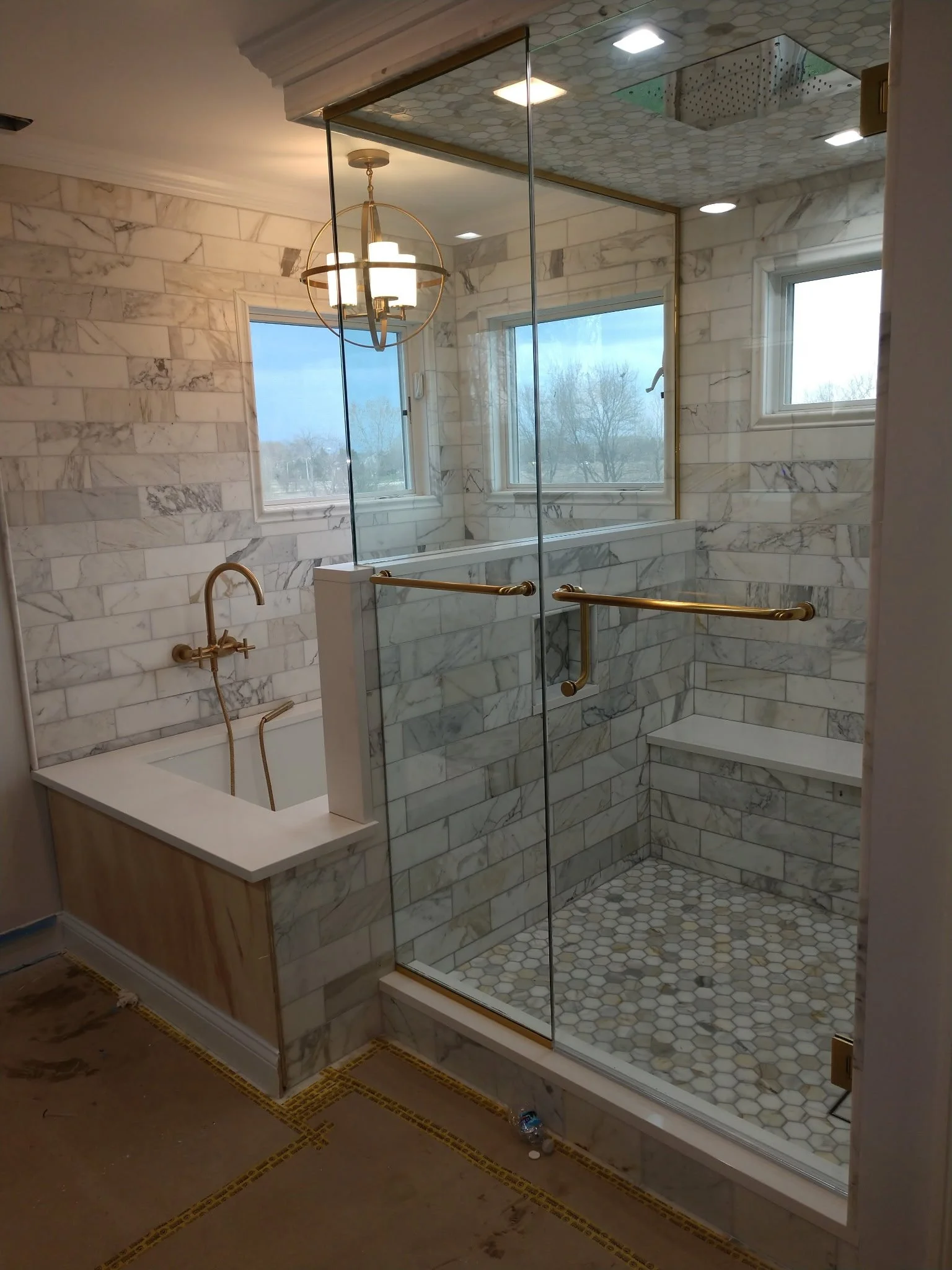 Luxury bathroom remodel featuring a marble tile shower, glass enclosure, brass fixtures, and custom finishes by HLS Construction.