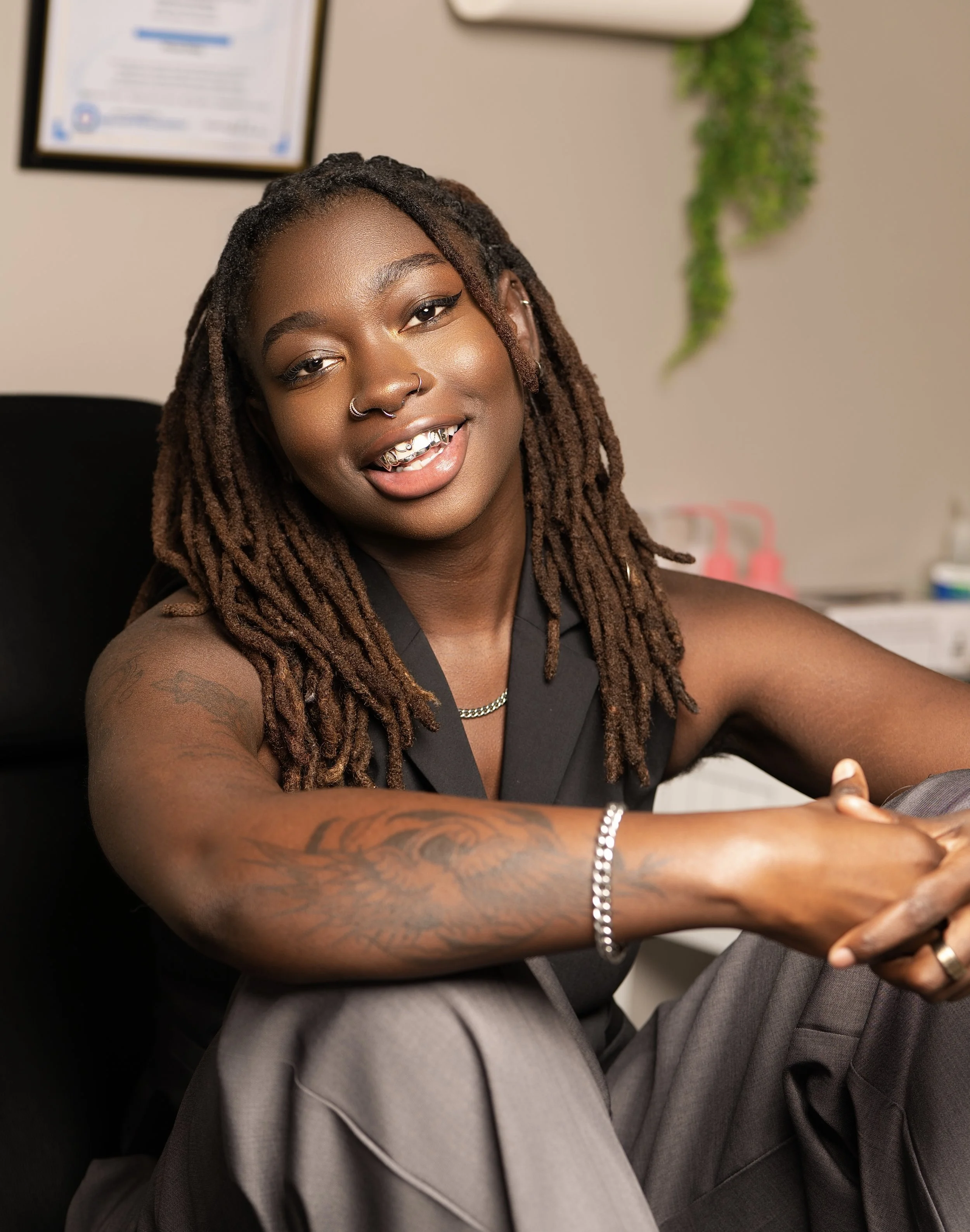 A woman with dreadlocks, multiple piercings, jewelry, and tattoos smiling in a professional setting.