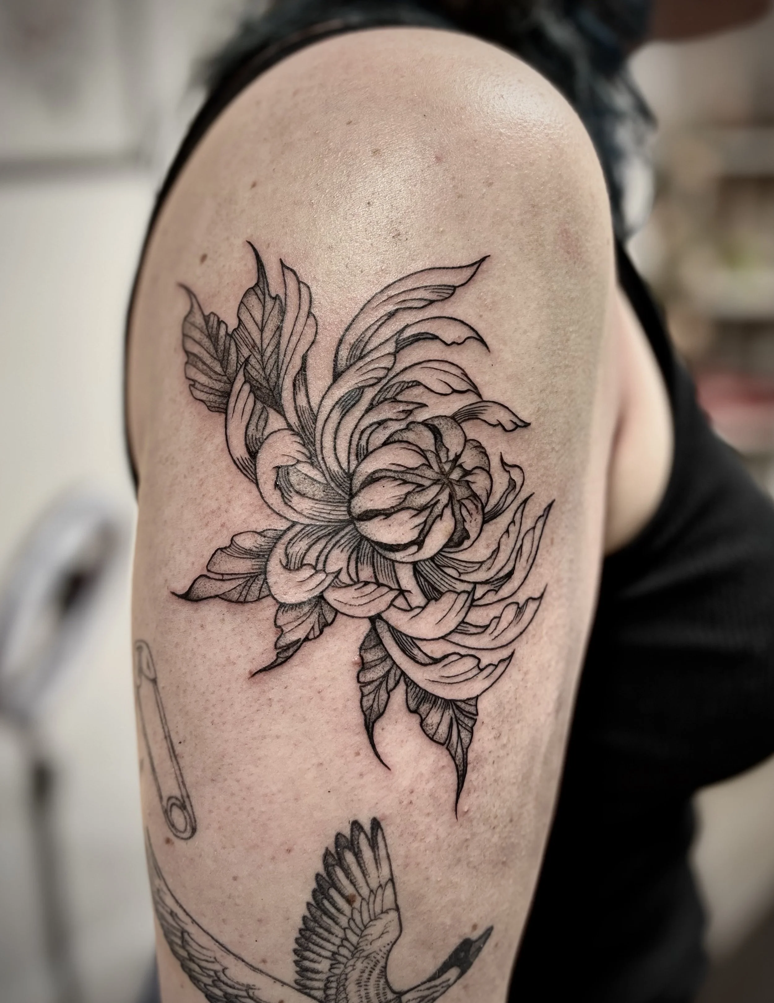 A black and gray floral tattoo on a person's upper arm, featuring detailed petals and leaves, with part of a phrase or word below it.