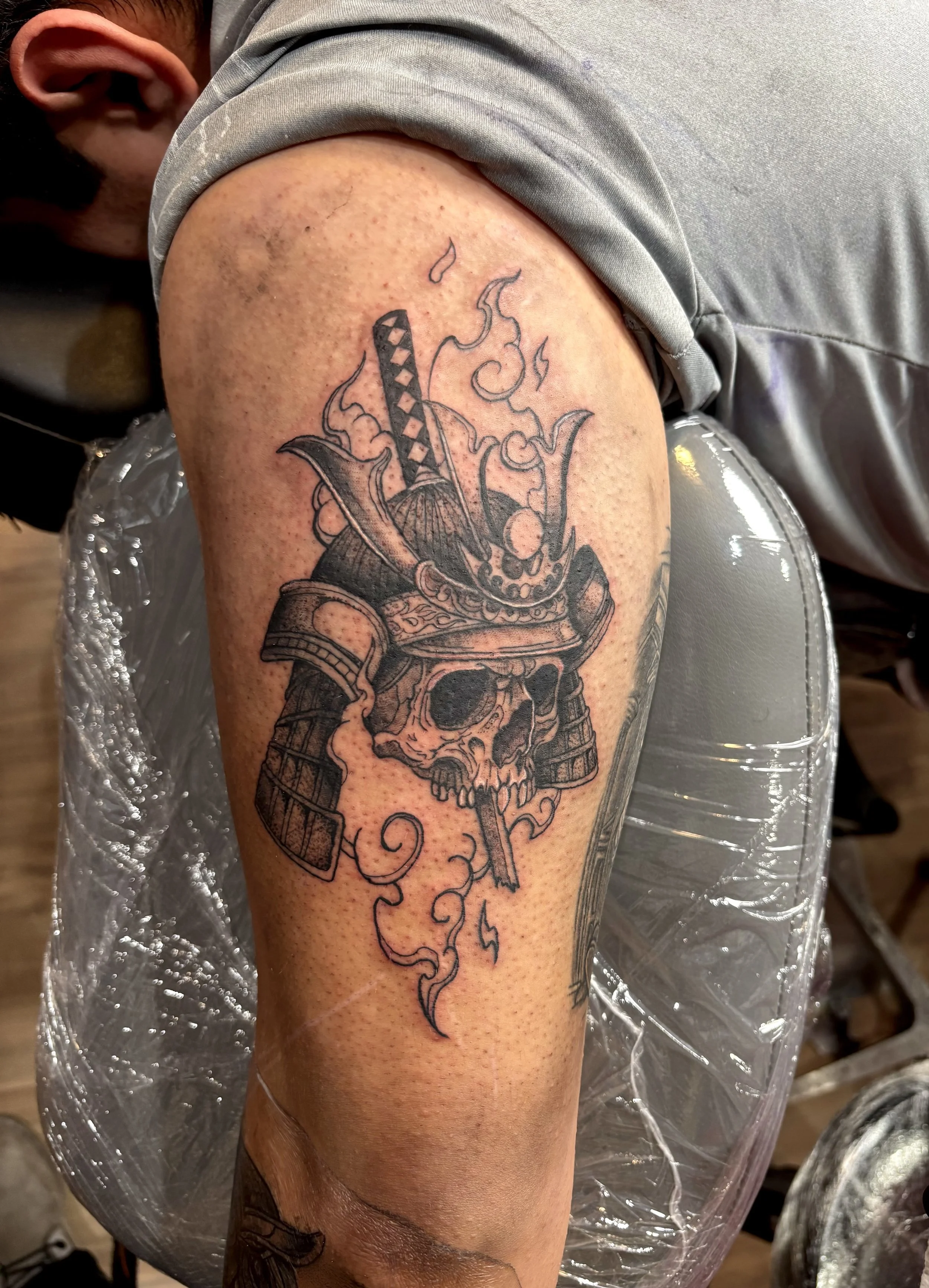 Tattoo of a skull with a sword piercing through it, with smoke and flame details around