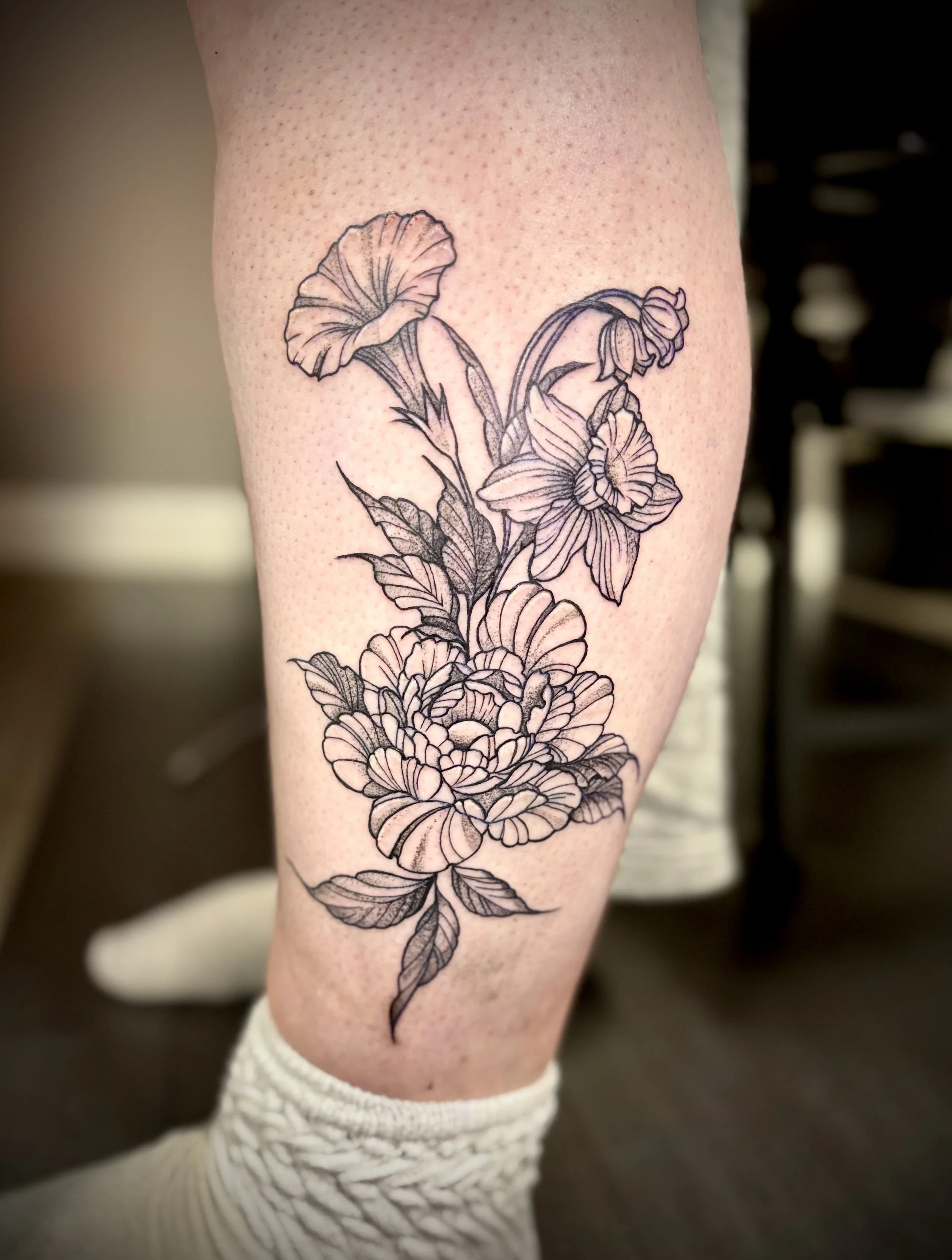 A black and gray floral tattoo on the person's leg, featuring detailed and intricate flowers and leaves.