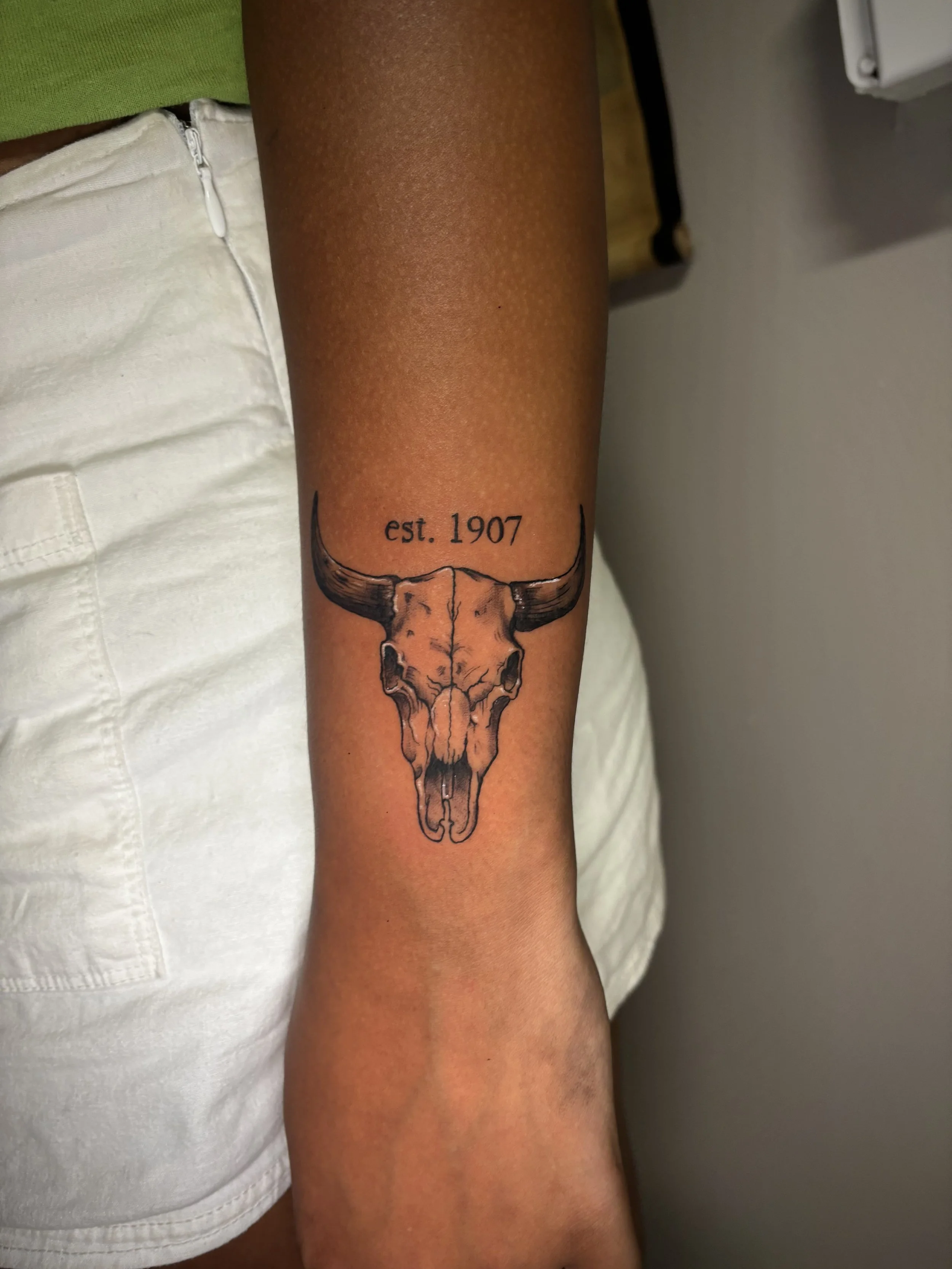 Tattoo of a longhorn skull with the text 'est. 1907' on the person's arm.