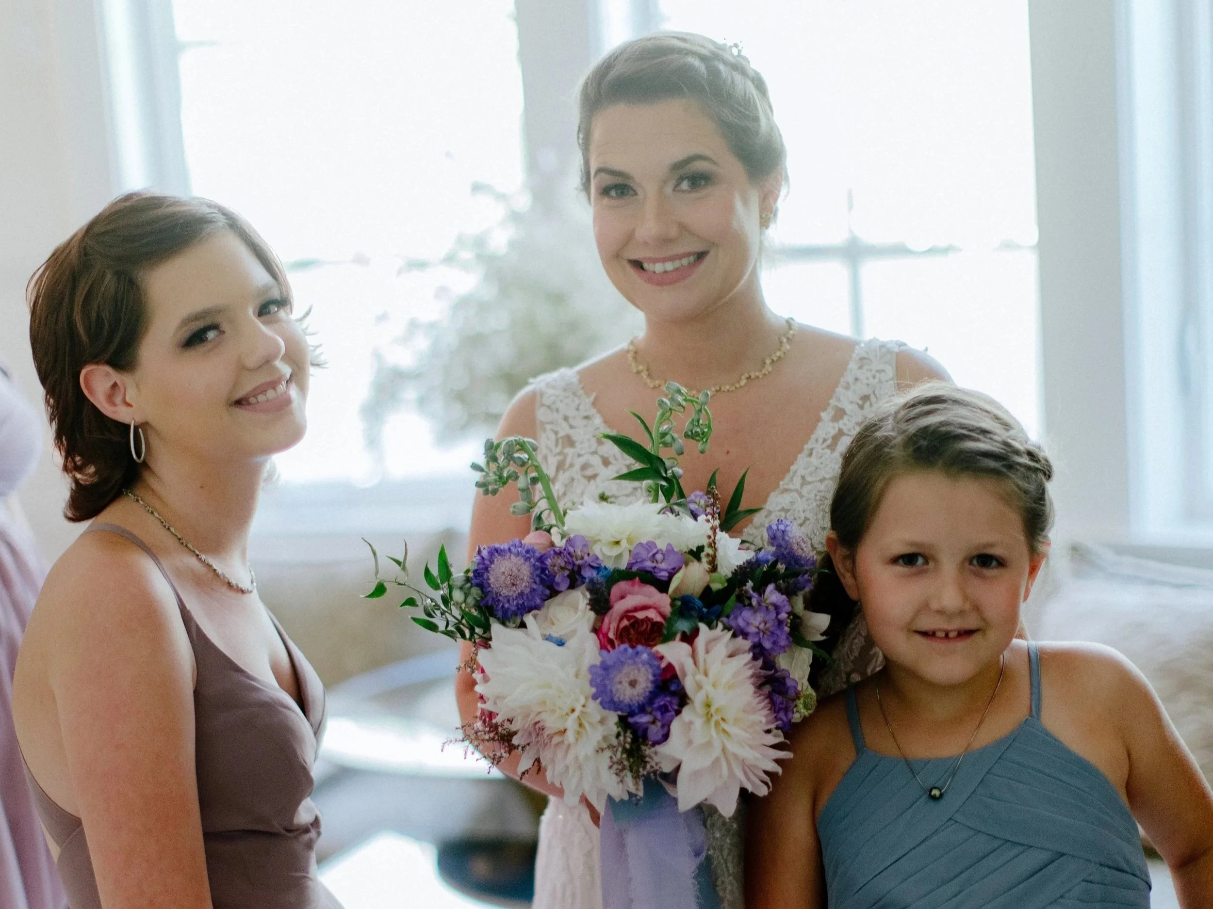 Women and children at a celebration, centerpiece of flowers, bright background with large windows.