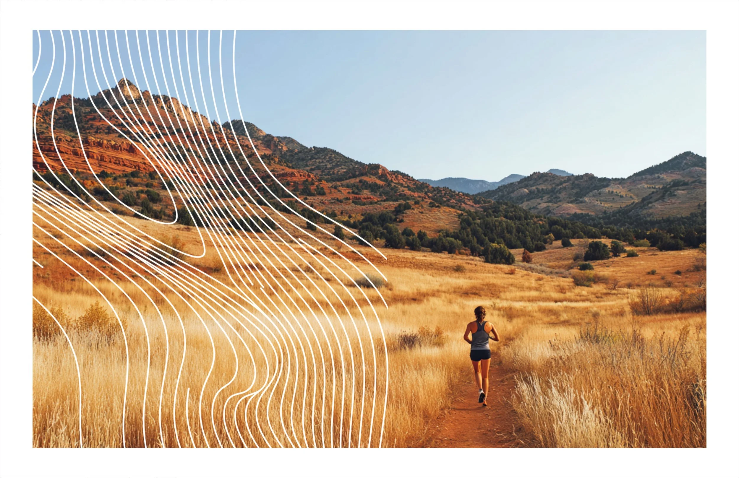 A woman running on a dirt trail through a golden grass field with mountains and clear blue sky in the background.