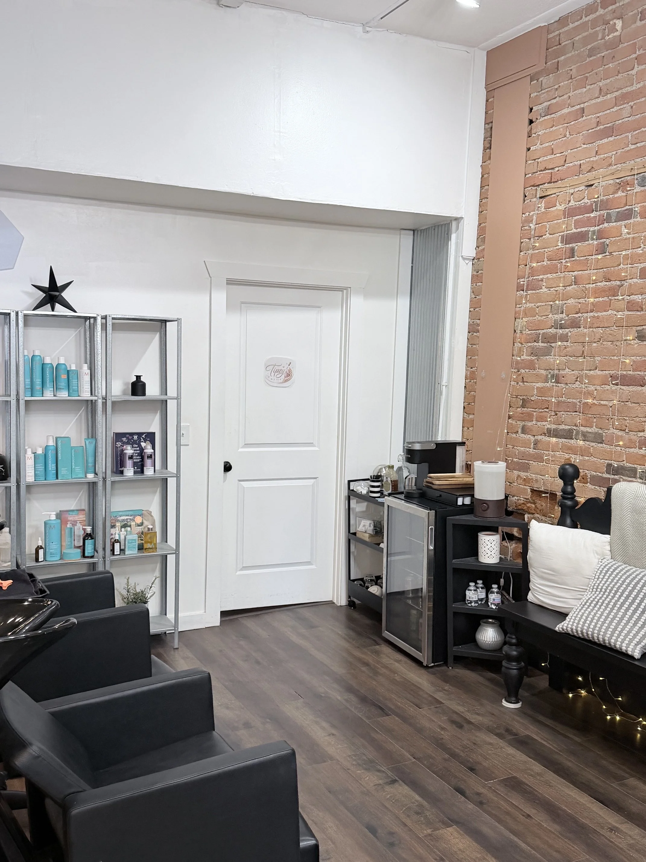 Interior of a salon or spa with black chairs, white walls, a brick accent wall, and shelves with hair and skincare products.