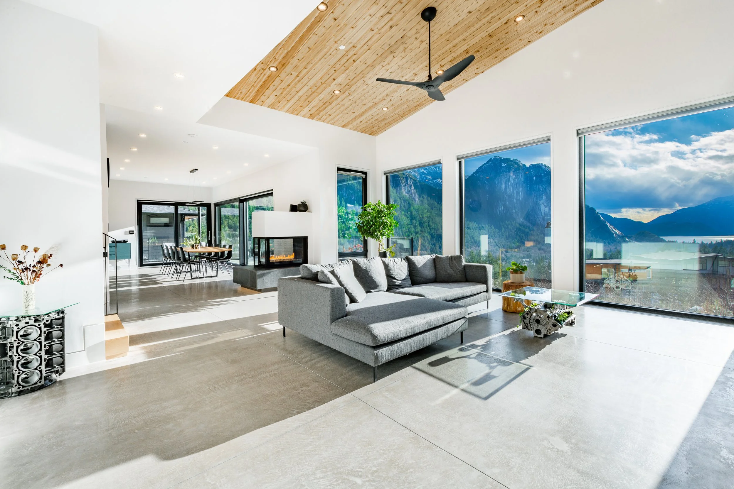 Modern living room with large windows displaying scenic mountain and lake view, gray sectional sofa, plants, and wood ceiling with ceiling fan mortgage broker mortgage services refinance renewal
