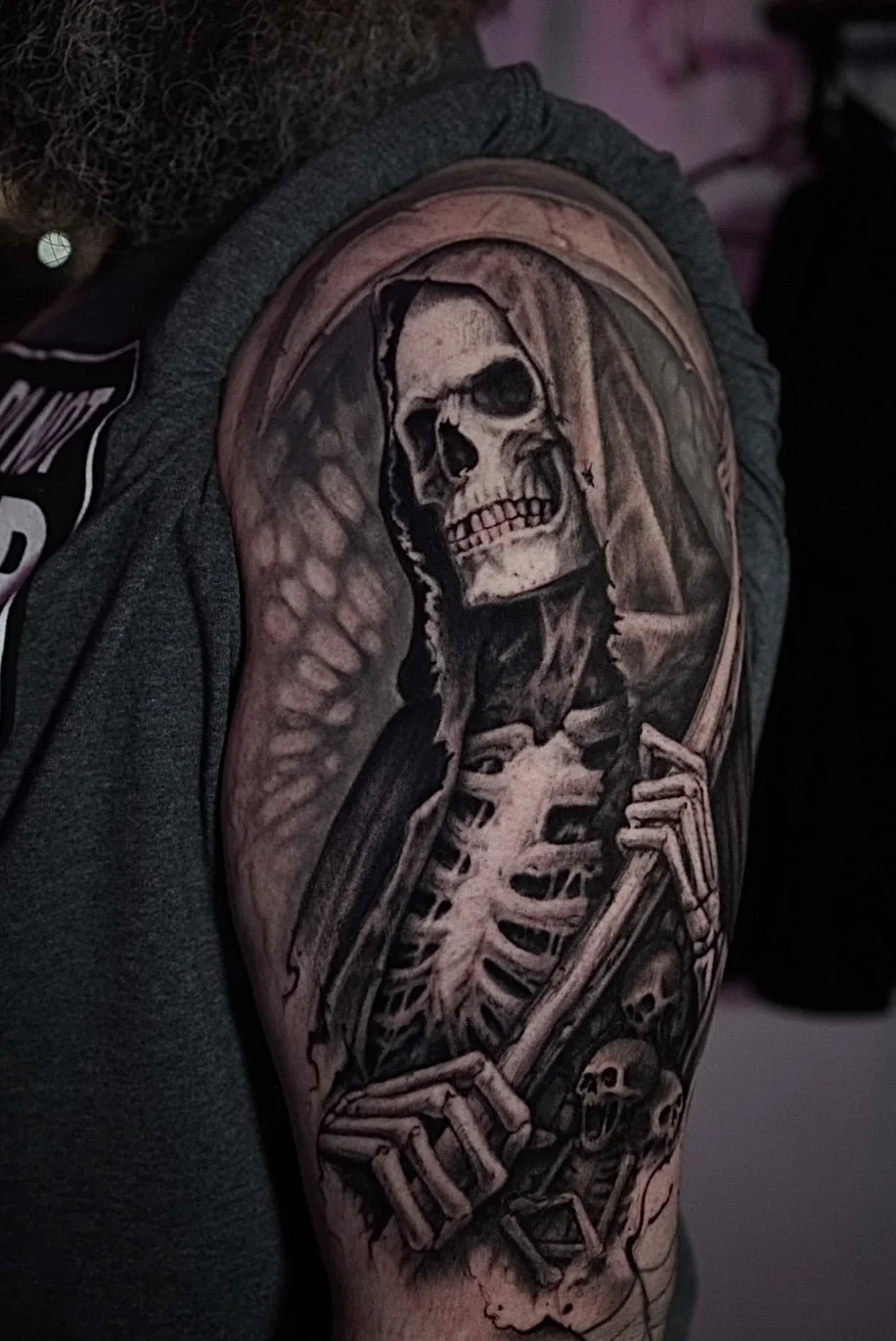 Black-and-gray Grim Reaper, scythe and skulls upper-arm tattoo by Luis Dajer.