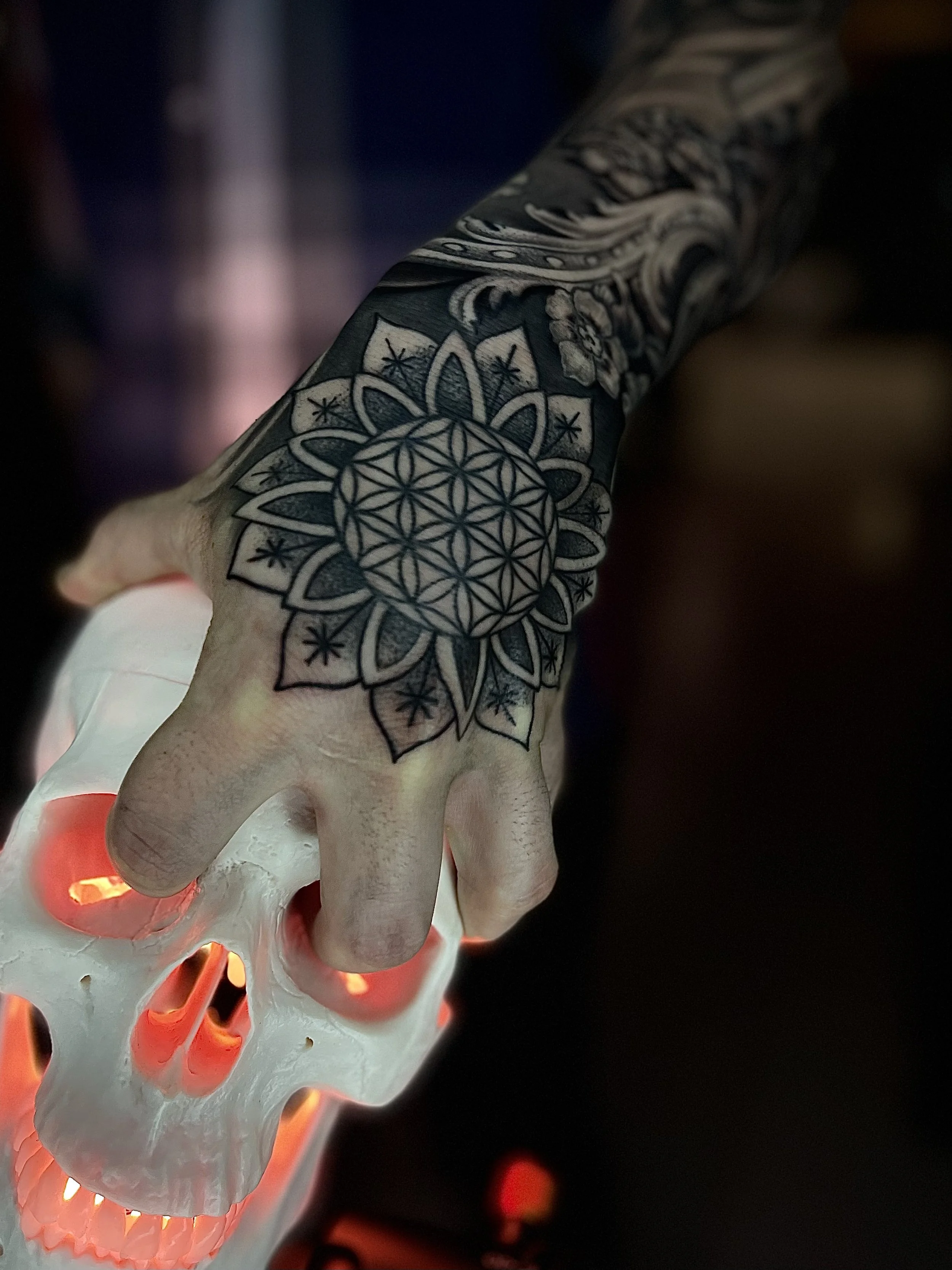 Tattooed hand holding a skull-shaped object illuminated by red light.