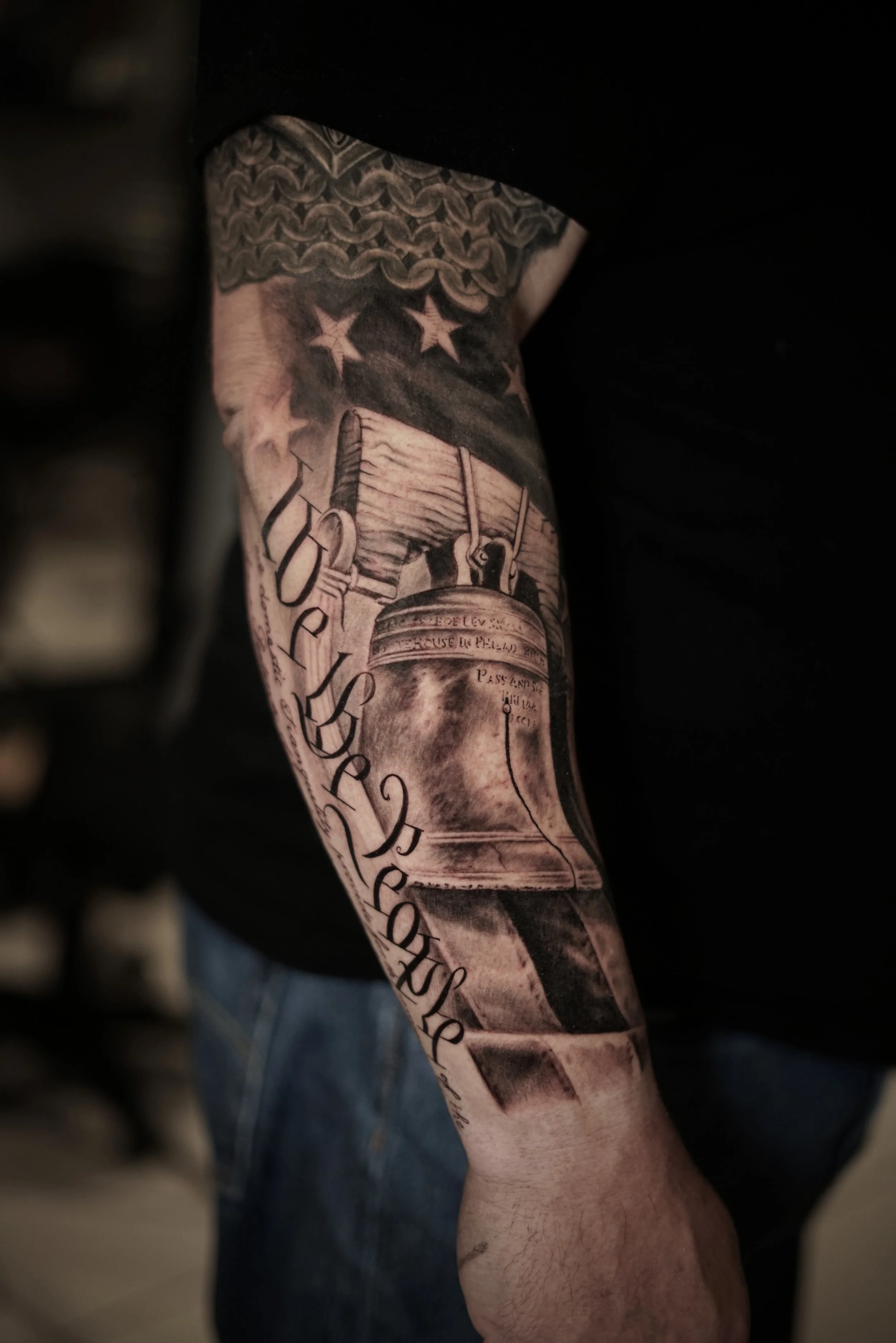Black-and-gray American flag, stars and dollar-bill forearm tattoo by Luis Dajer.