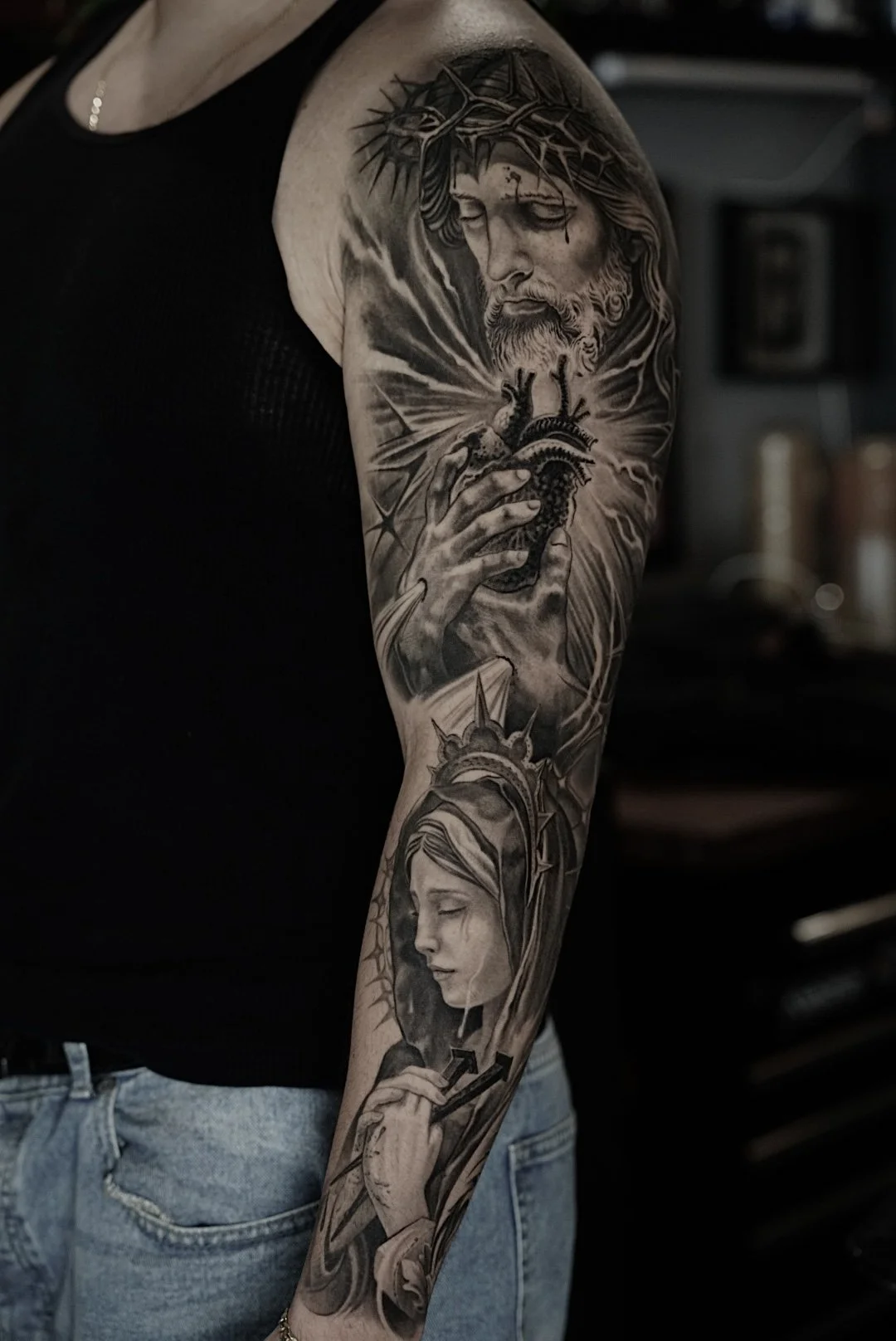 Black-and-gray religious sleeve tattoo with Jesus and a haloed woman at Black Craft Tattoo Collective in Charlotte, NC.