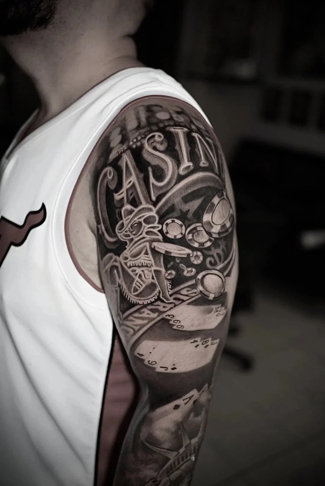 Black-and-gray poker chips, playing cards and PASS upper-arm tattoo by Luis Dajer.