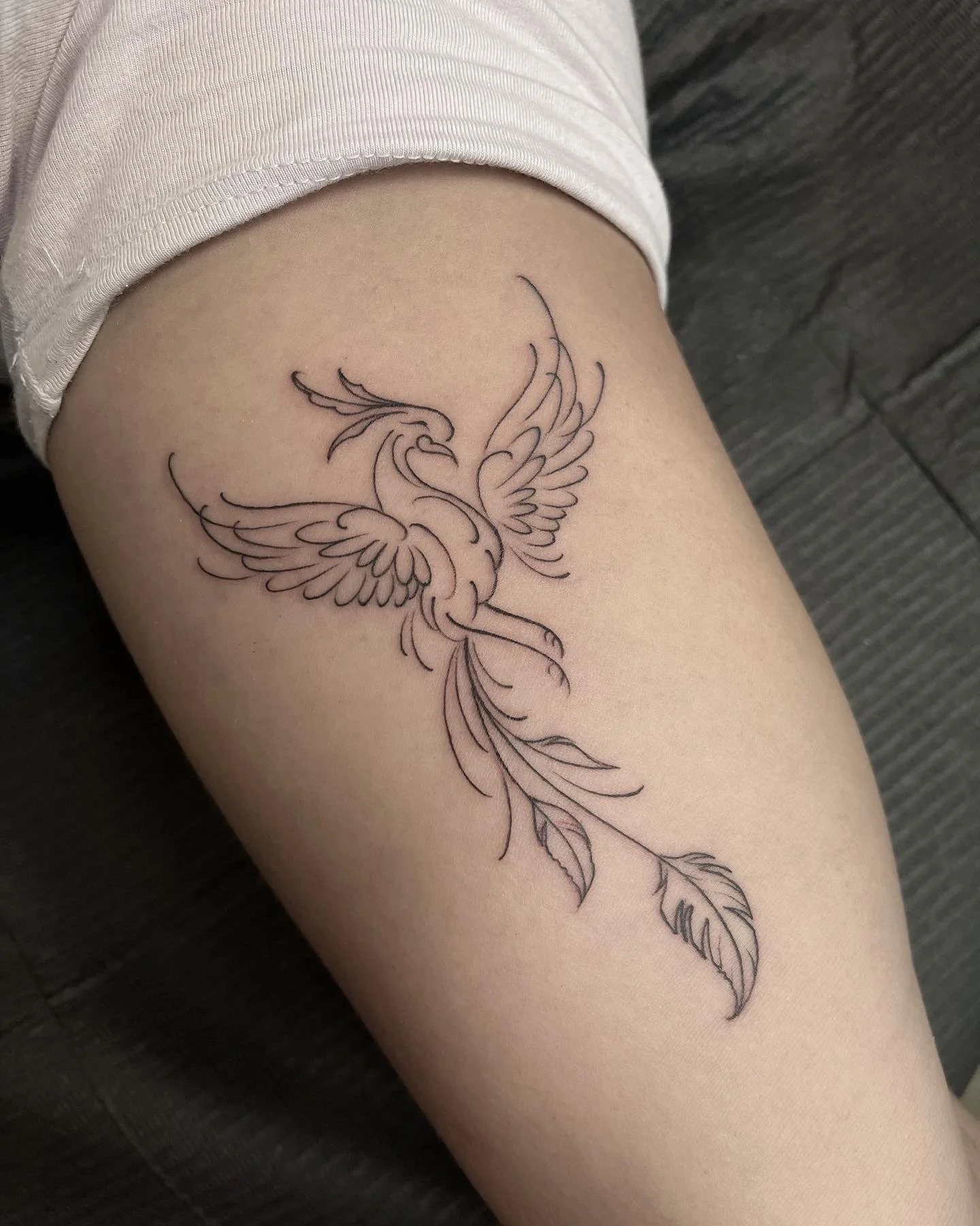 Fine-line bird with spread wings tattoo on the thigh.