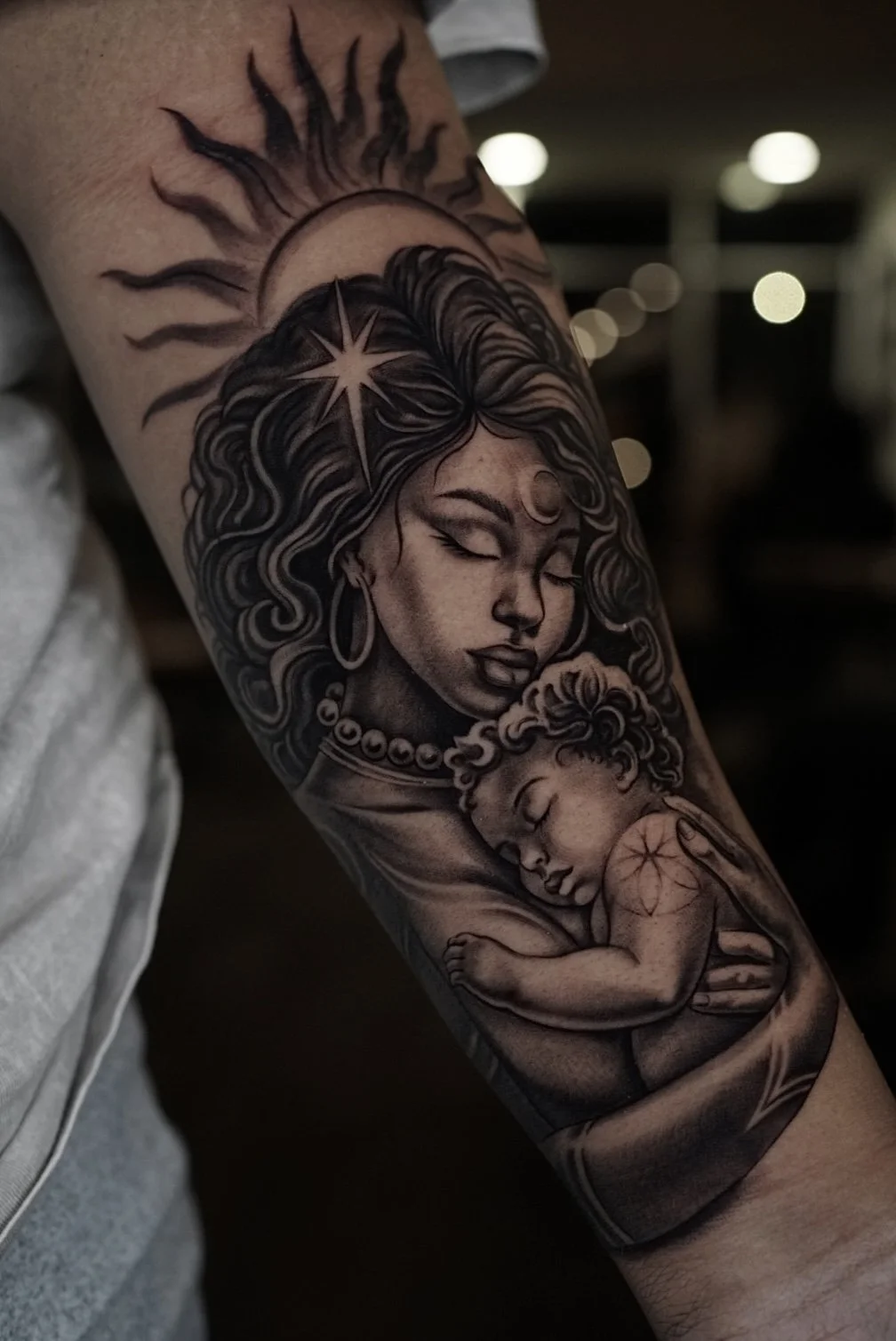 Black-and-gray mother holding a sleeping child with sun-and-moon details.