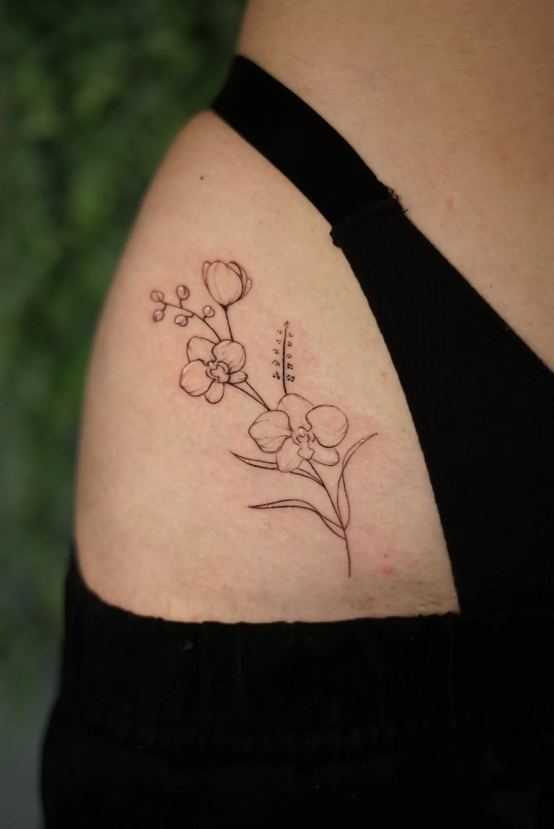 Fine-line floral and Braille upper-arm tattoo by Luis Dajer.