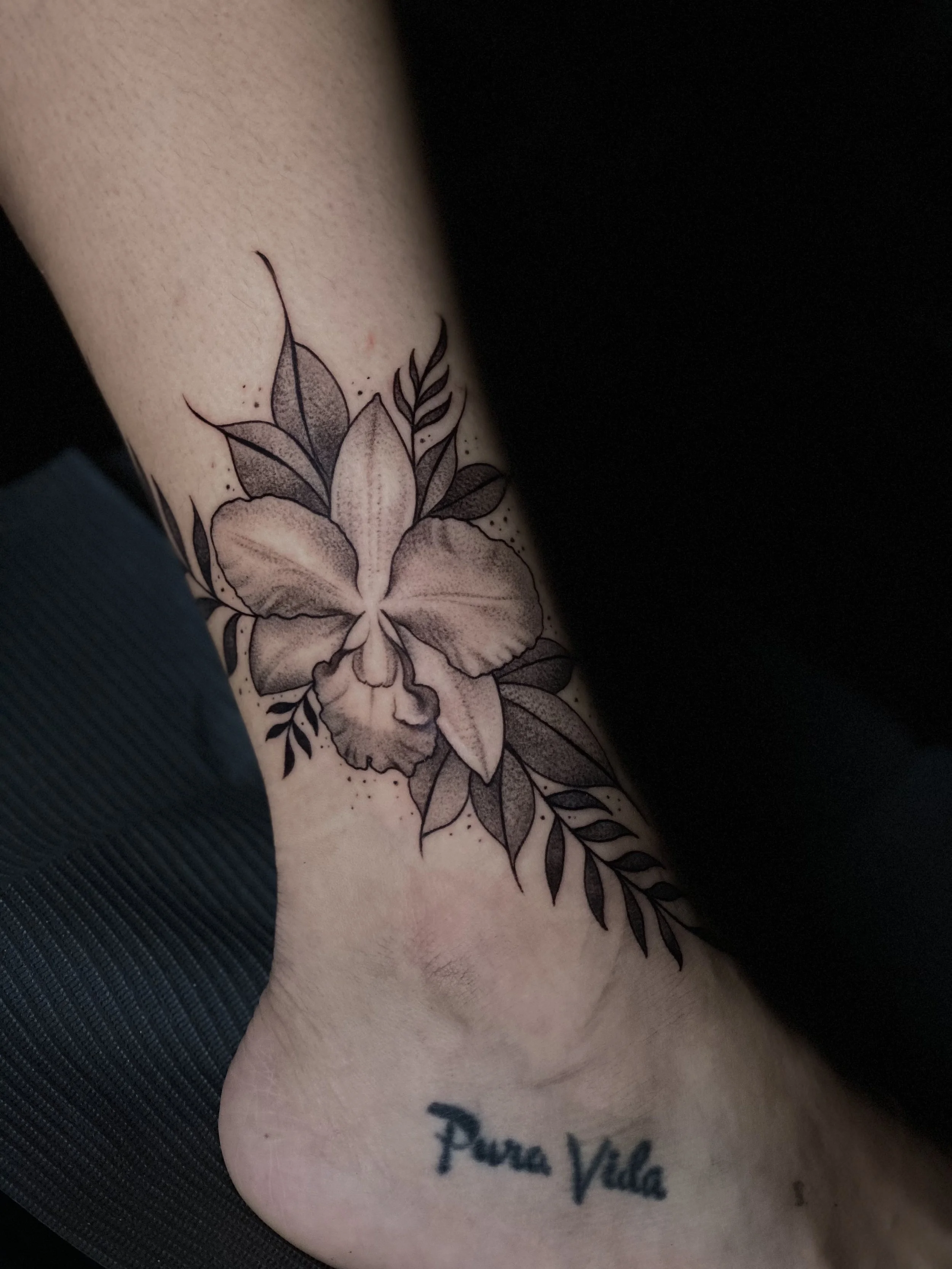 Floral arm tattoo with leaves and Pura Vida script at Black Craft Tattoo Collective.