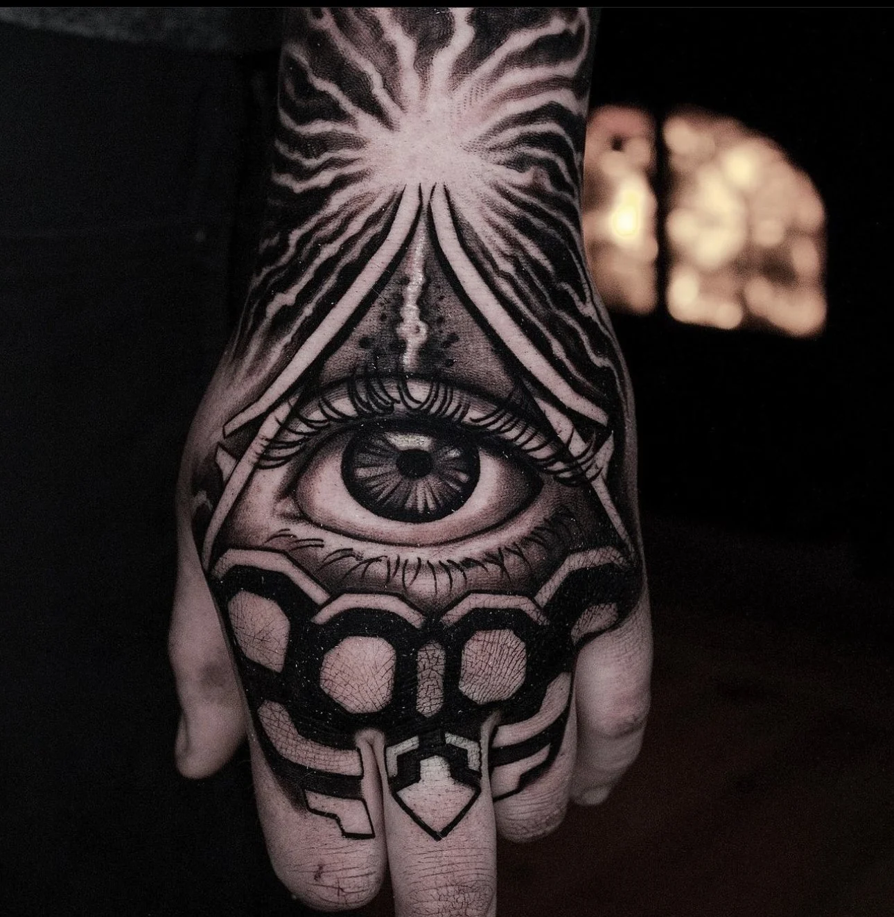Black-and-gray geometric eye tattoo across the hand and forearm.