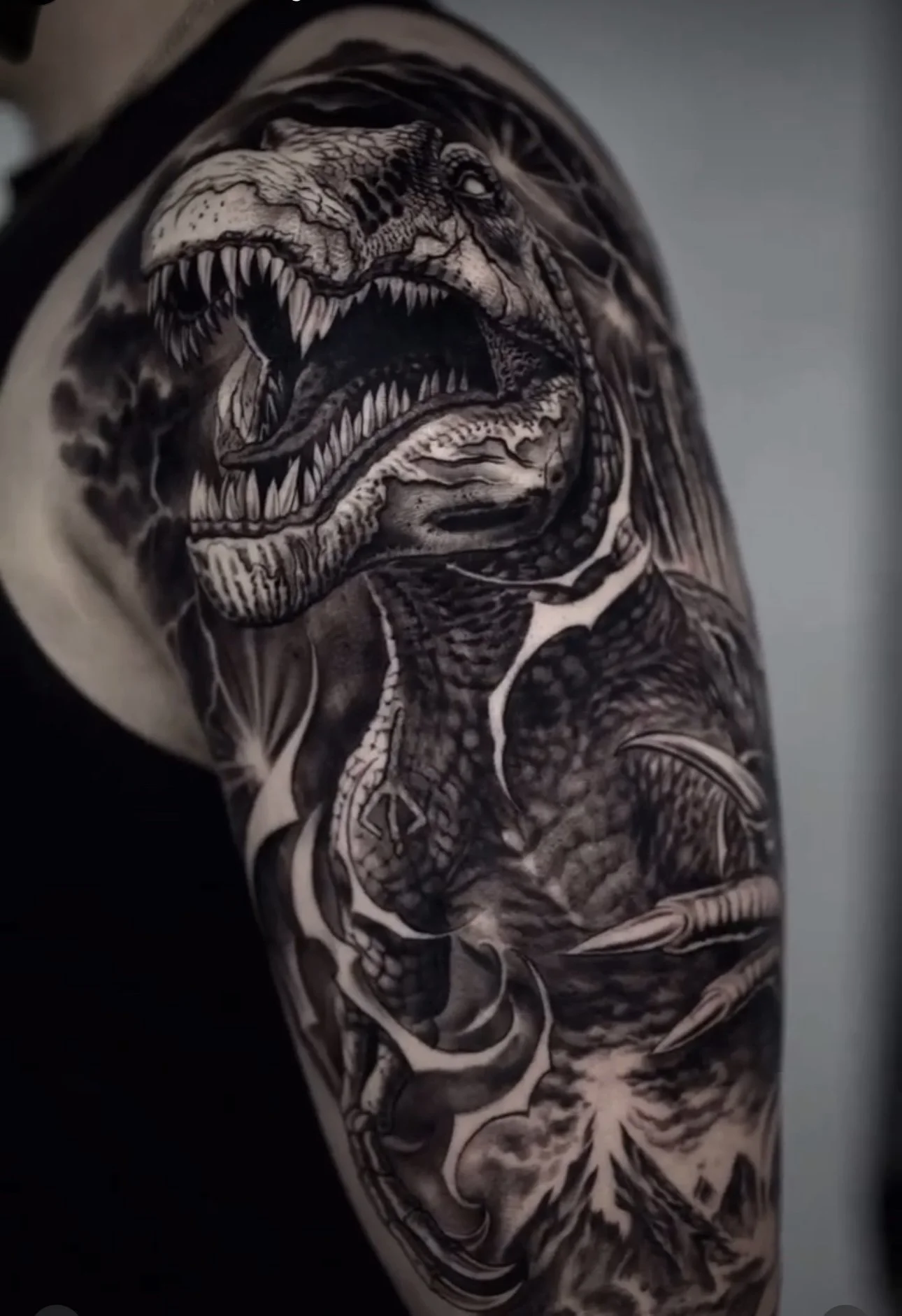 Black-and-gray roaring T-Rex tattoo on the upper arm at Black Craft Tattoo Collective.