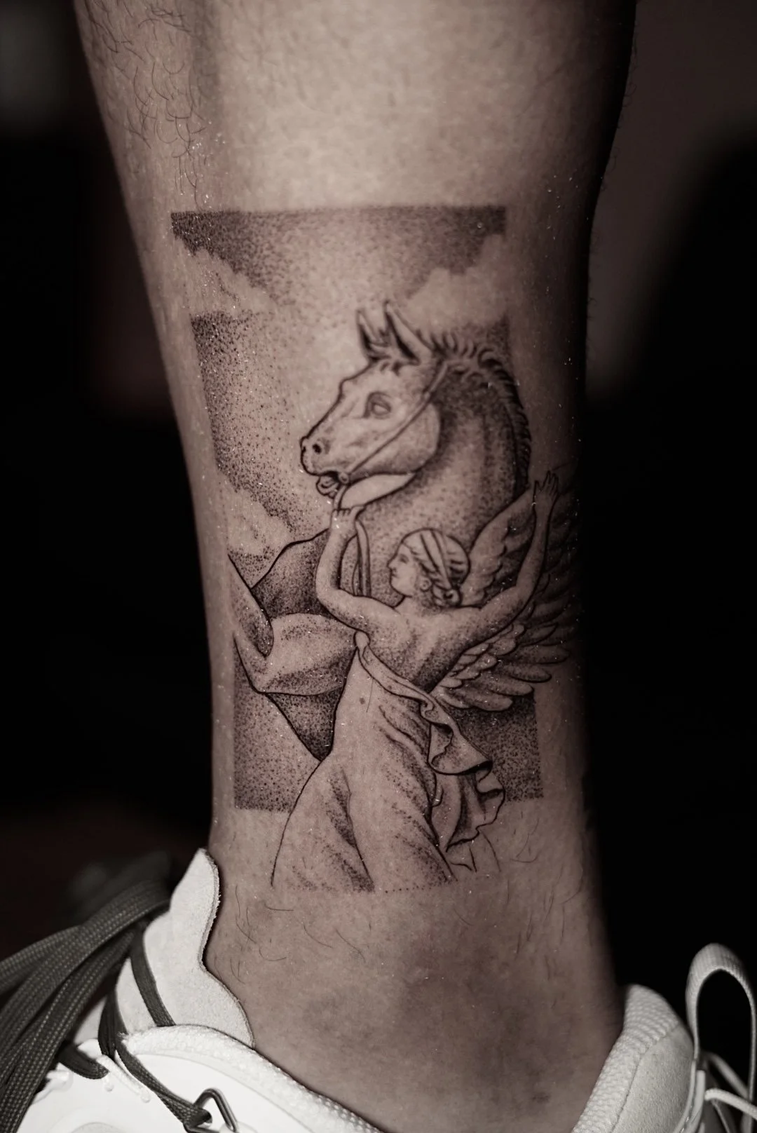 Fine-line winged woman holding a unicorn head tattoo by Luis Dajer.