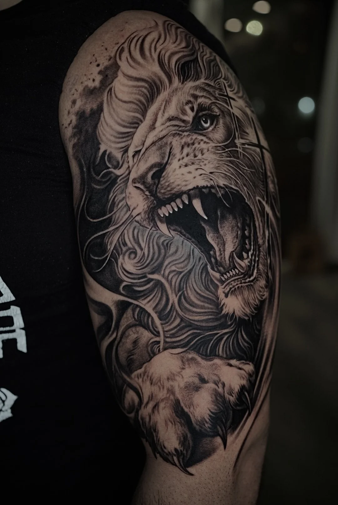Realistic black-and-gray roaring lion upper-arm tattoo.