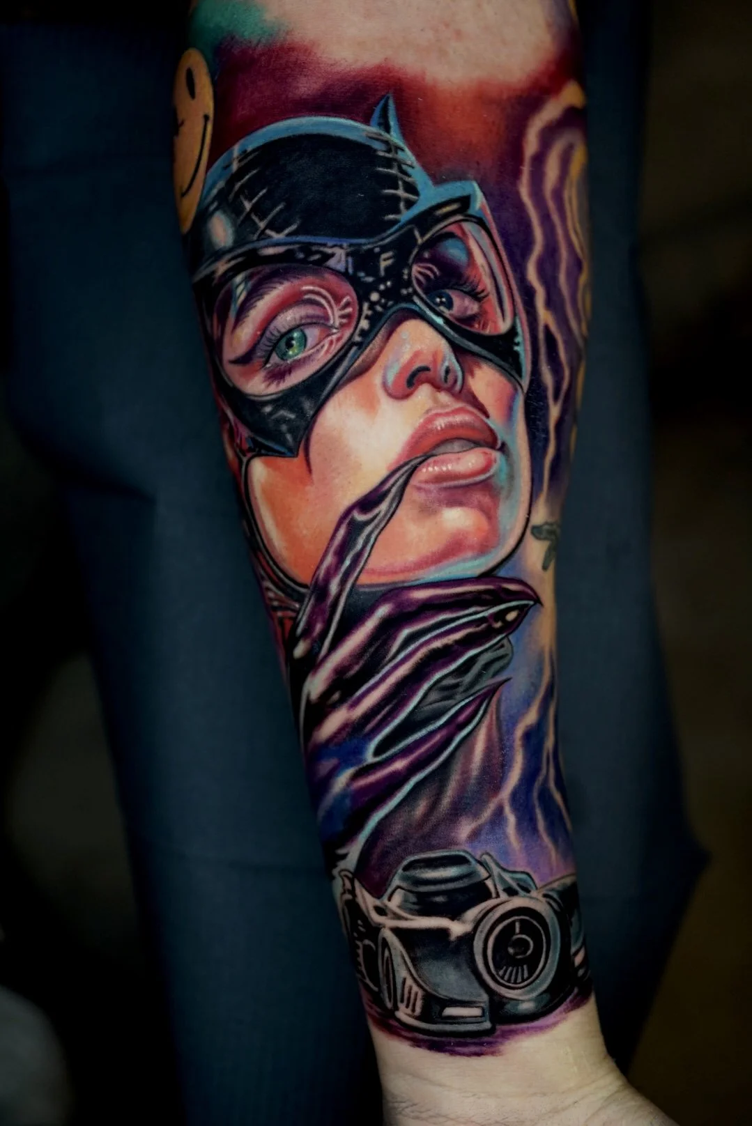 Vibrant color masked-woman portrait with green eyes and camera tattoo.