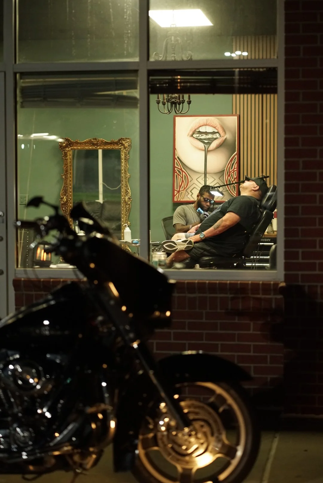 Tattoo session viewed through the Black Craft studio window with a motorcycle outside.