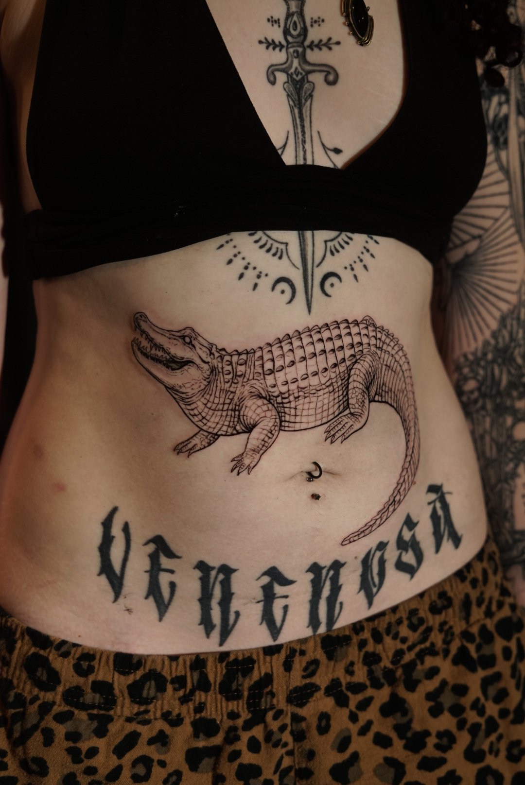 Black-and-gray crocodile stomach tattoo with dagger and Gothic lettering by Luis Dajer.