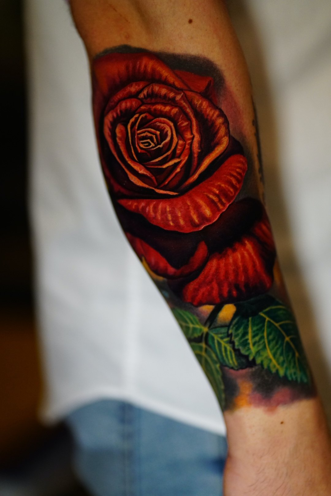 Vibrant red rose and green leaves arm tattoo at Black Craft Tattoo Collective.