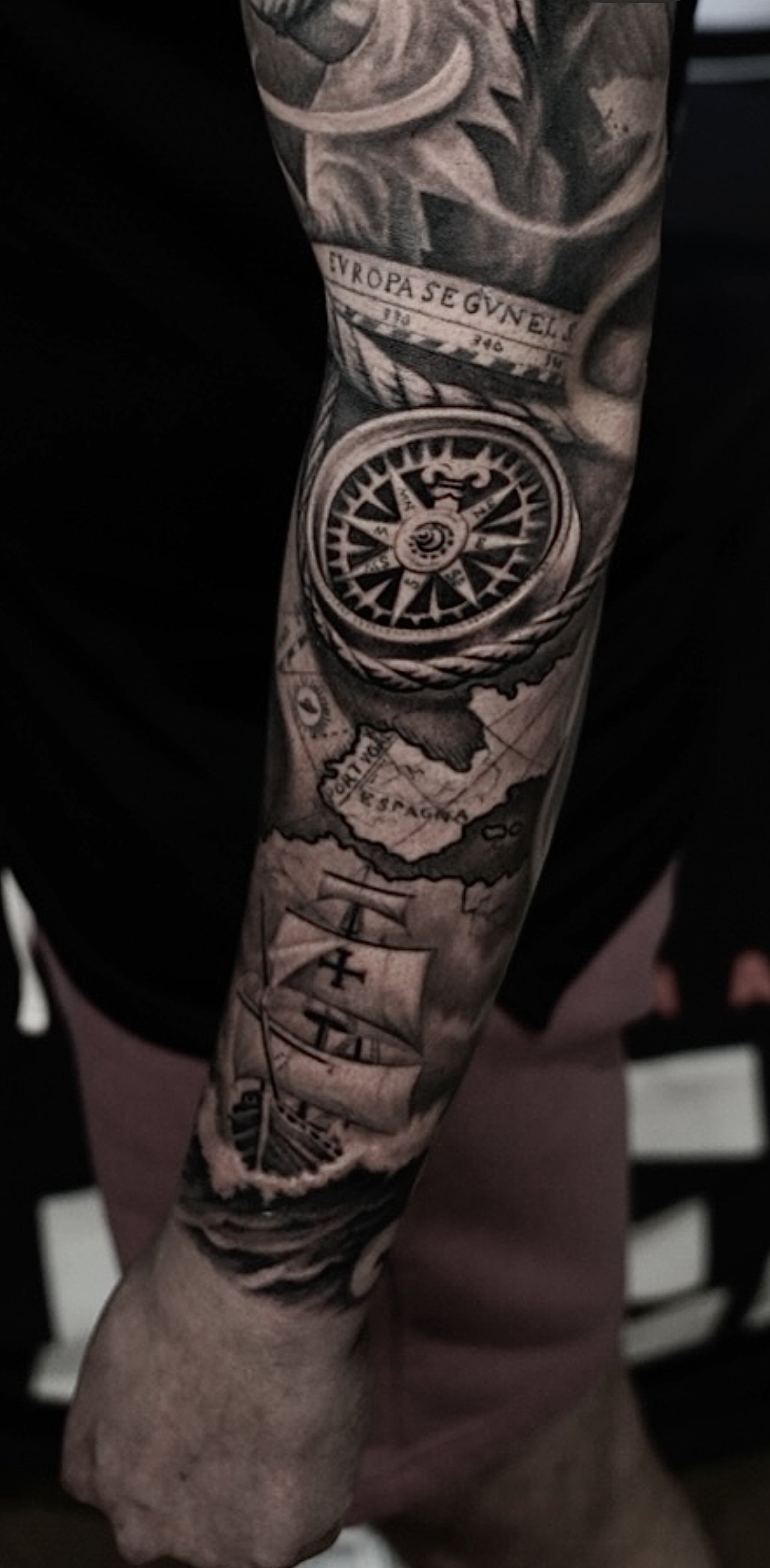 Compass, map of Spain and Latin-script arm tattoo by Luis Dajer in Charlotte, NC.