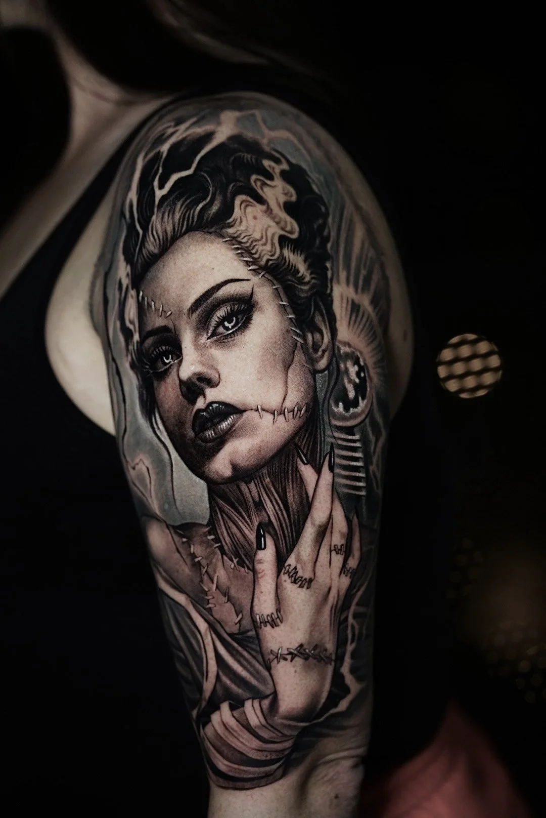 Black-and-gray stitched-woman portrait tattoo on the upper arm.