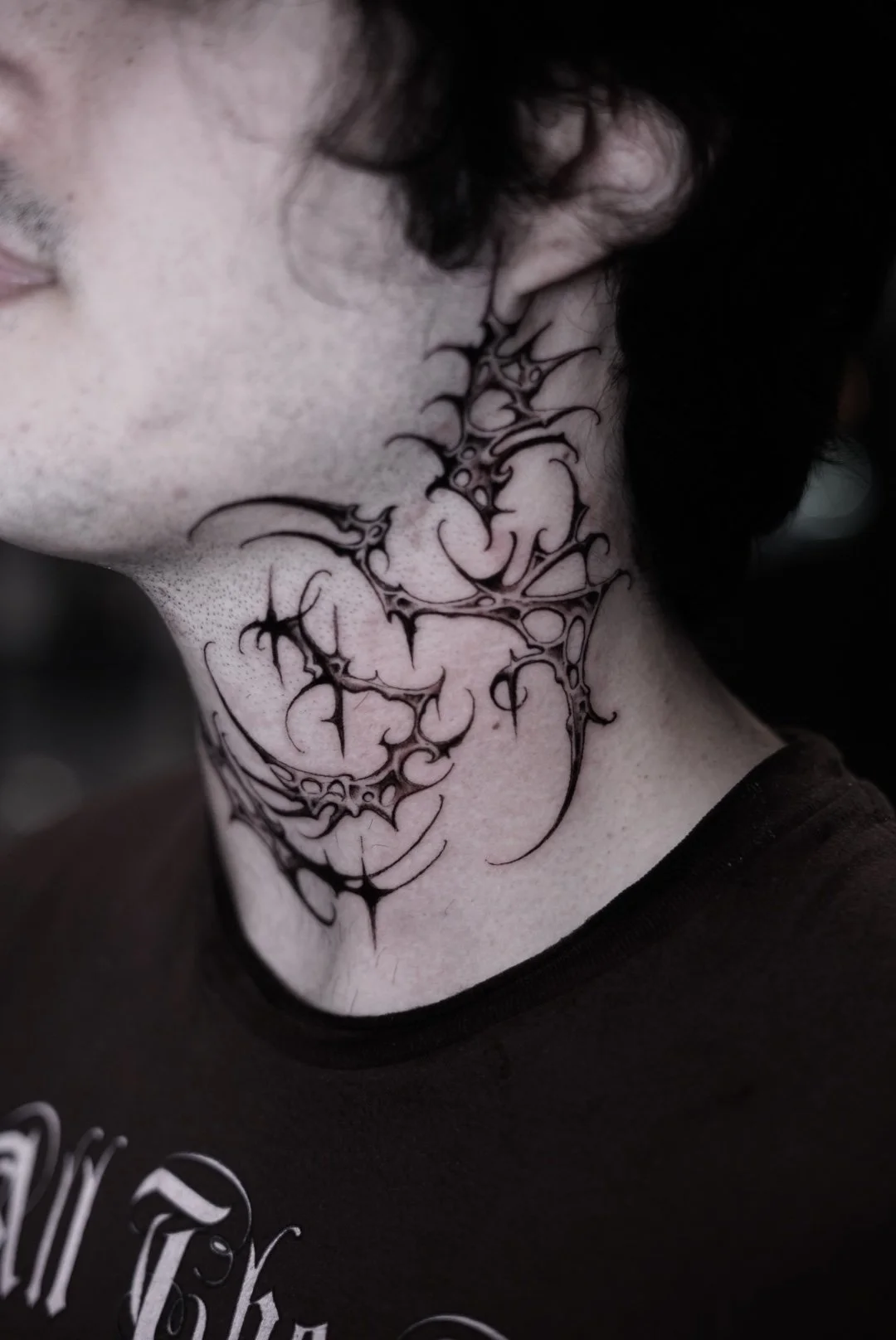Black tribal neck and chin tattoo with sharp flowing lines by Luis Dajer.