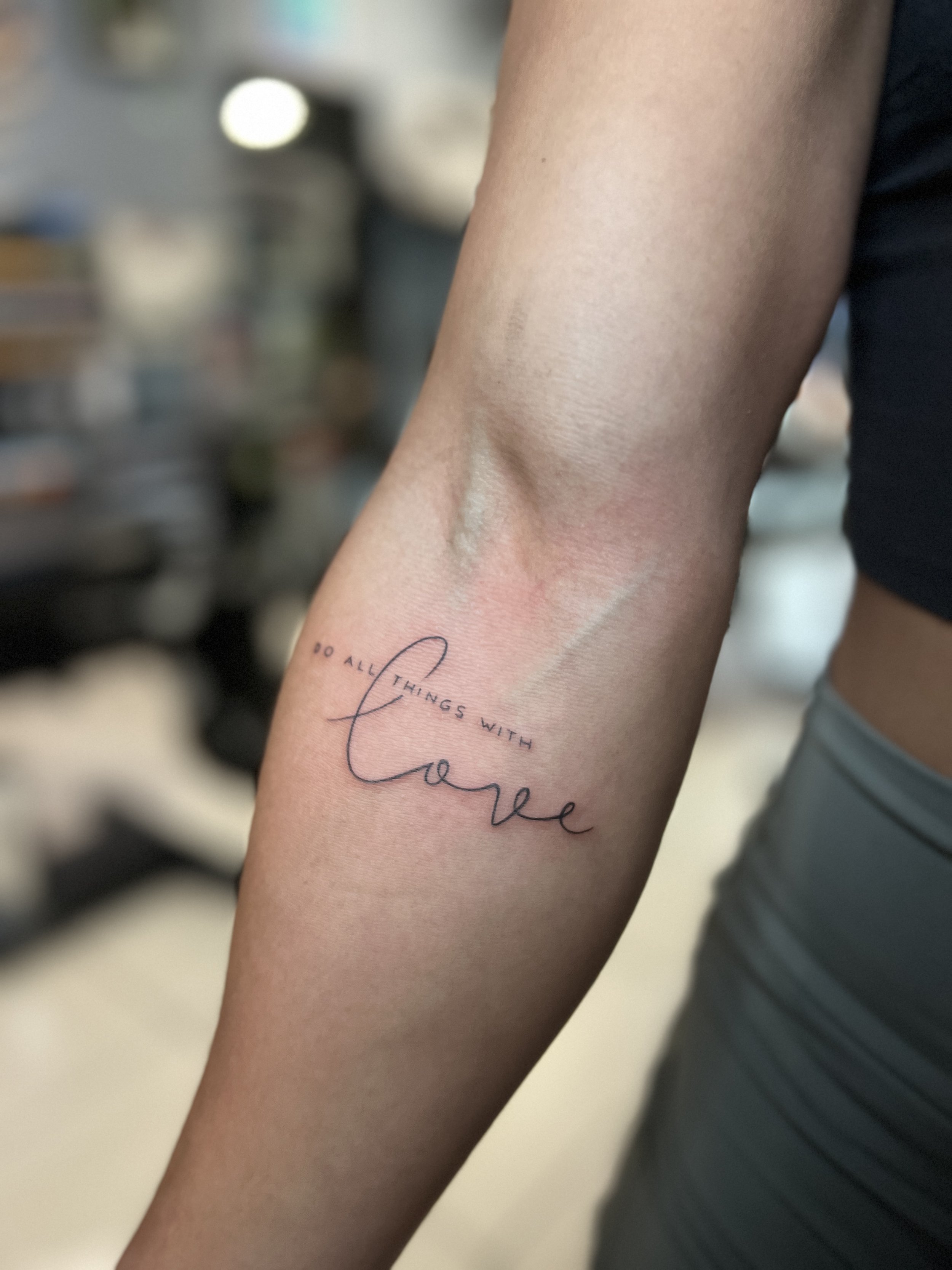 Fine-line do all things with love script forearm tattoo by Luis Dajer.