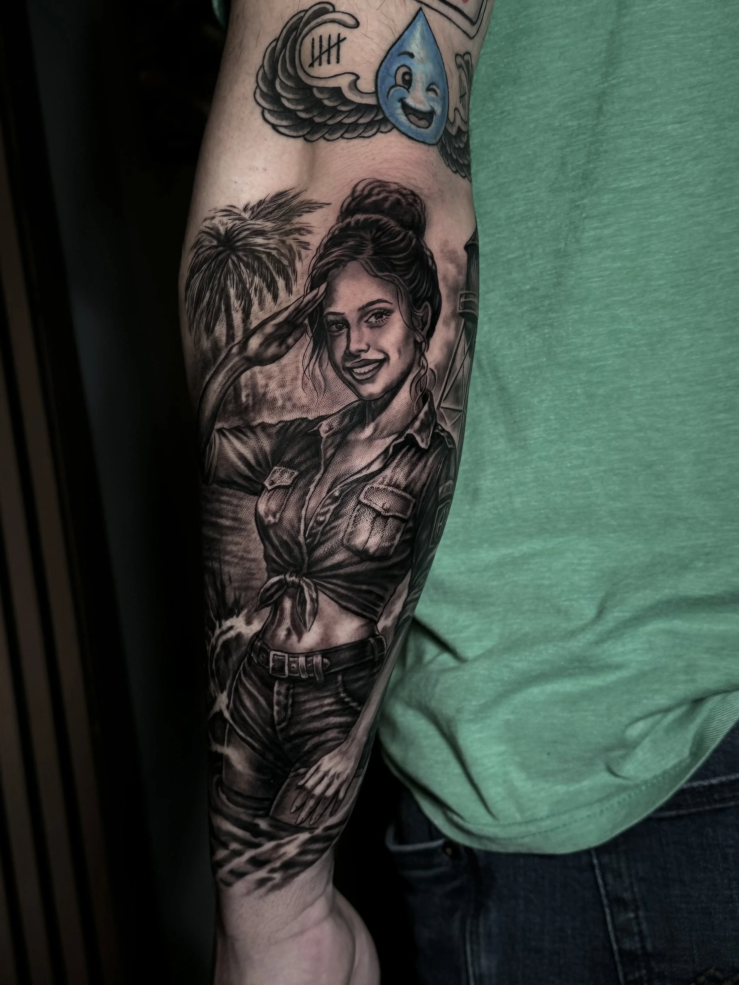 Color portrait tattoo of a saluting woman with palm trees on the upper arm.