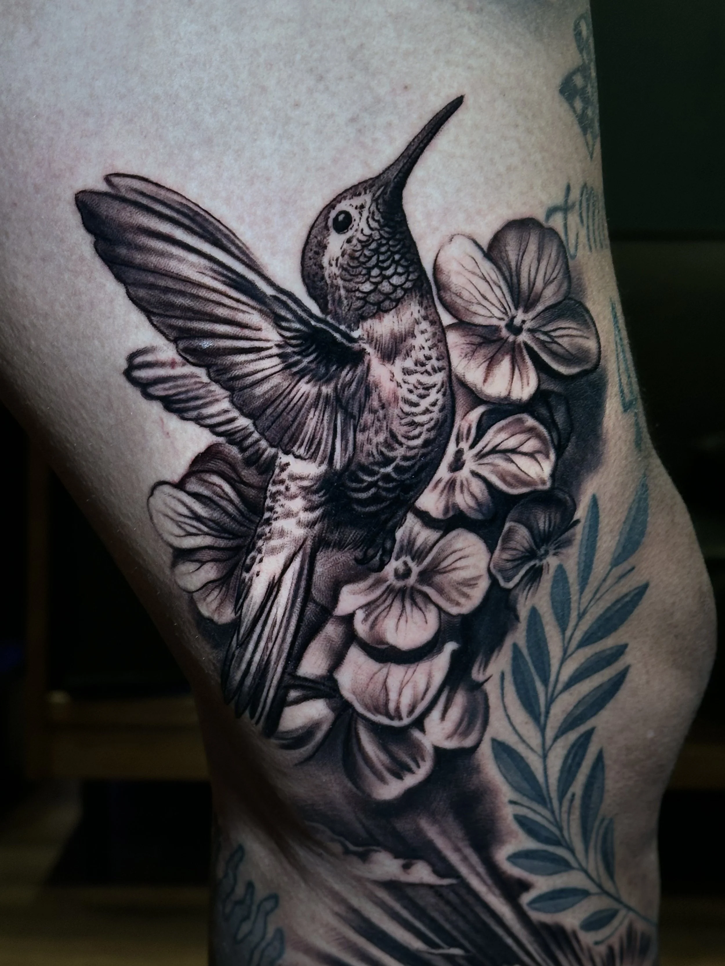 Black-and-gray hummingbird and flower arm tattoo at Black Craft Tattoo Collective.