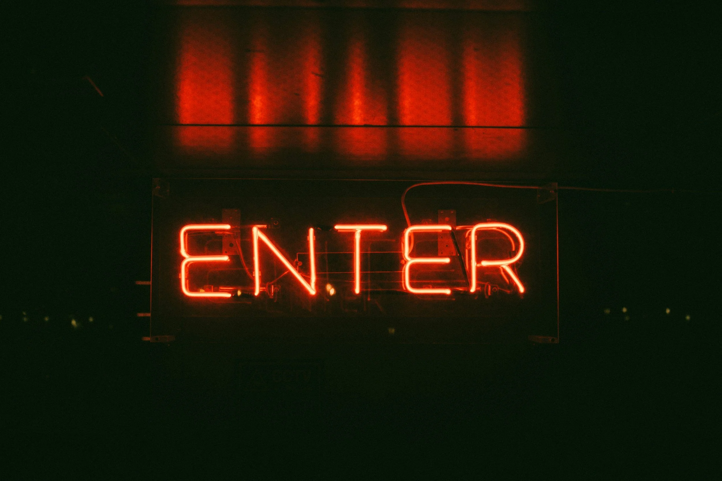 Red neon sign spelling 'ENTER' against a dark background.