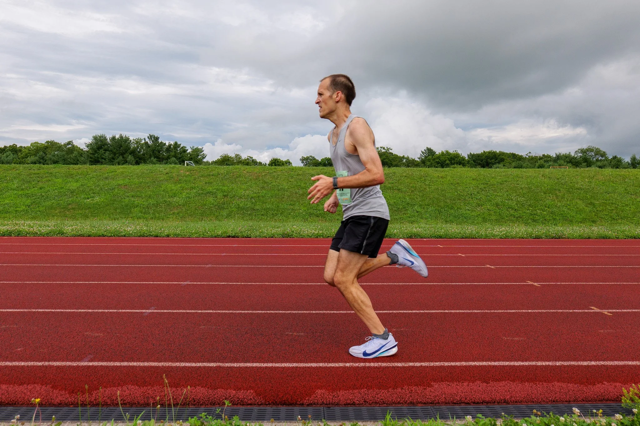 Man running on a red track field during overcast weather.