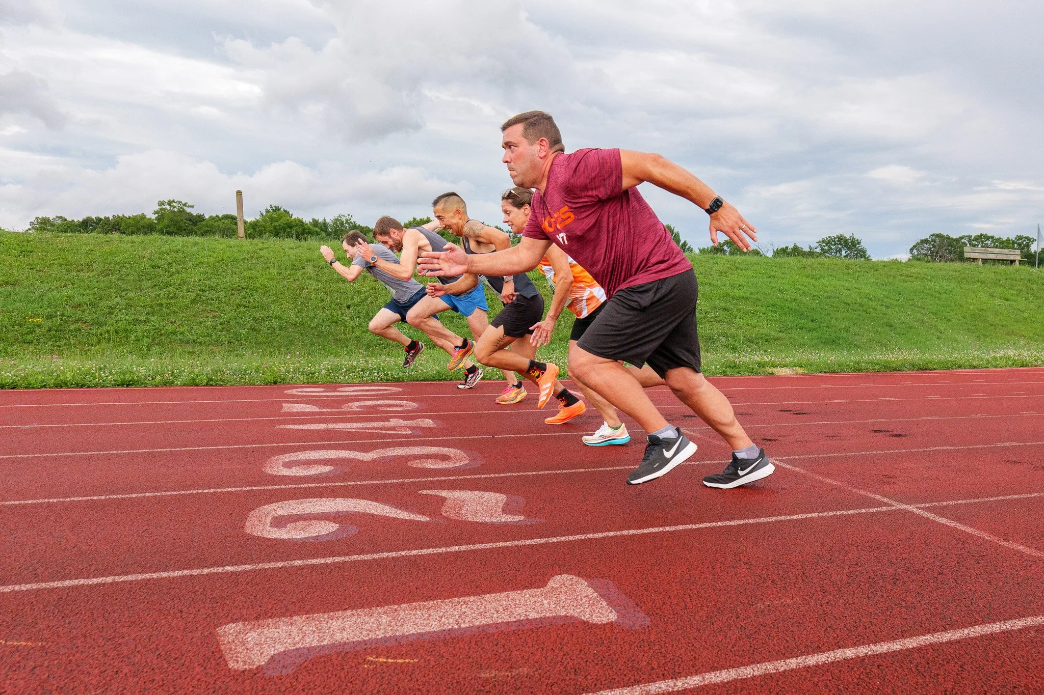 Group of runners at the starting line of a track race on a cloudy day.