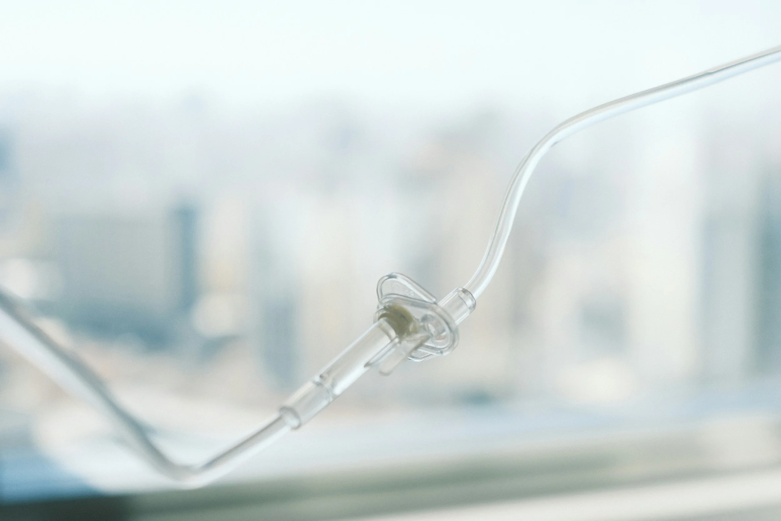Close-up of a clear medical IV drip tubing hanging with a blurred cityscape in the background.