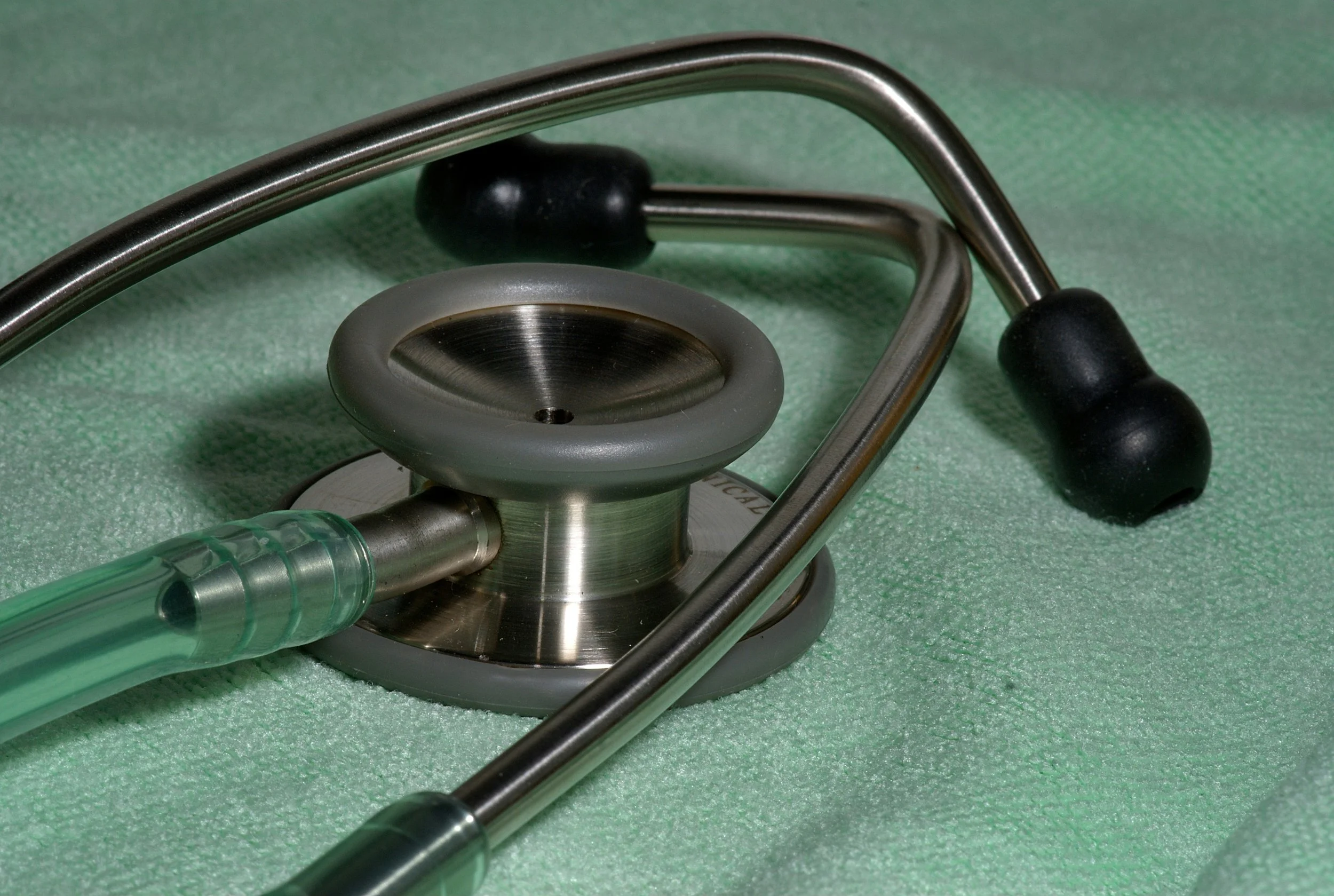 Stethoscope with metal chest piece and ear tips on a green textured background.