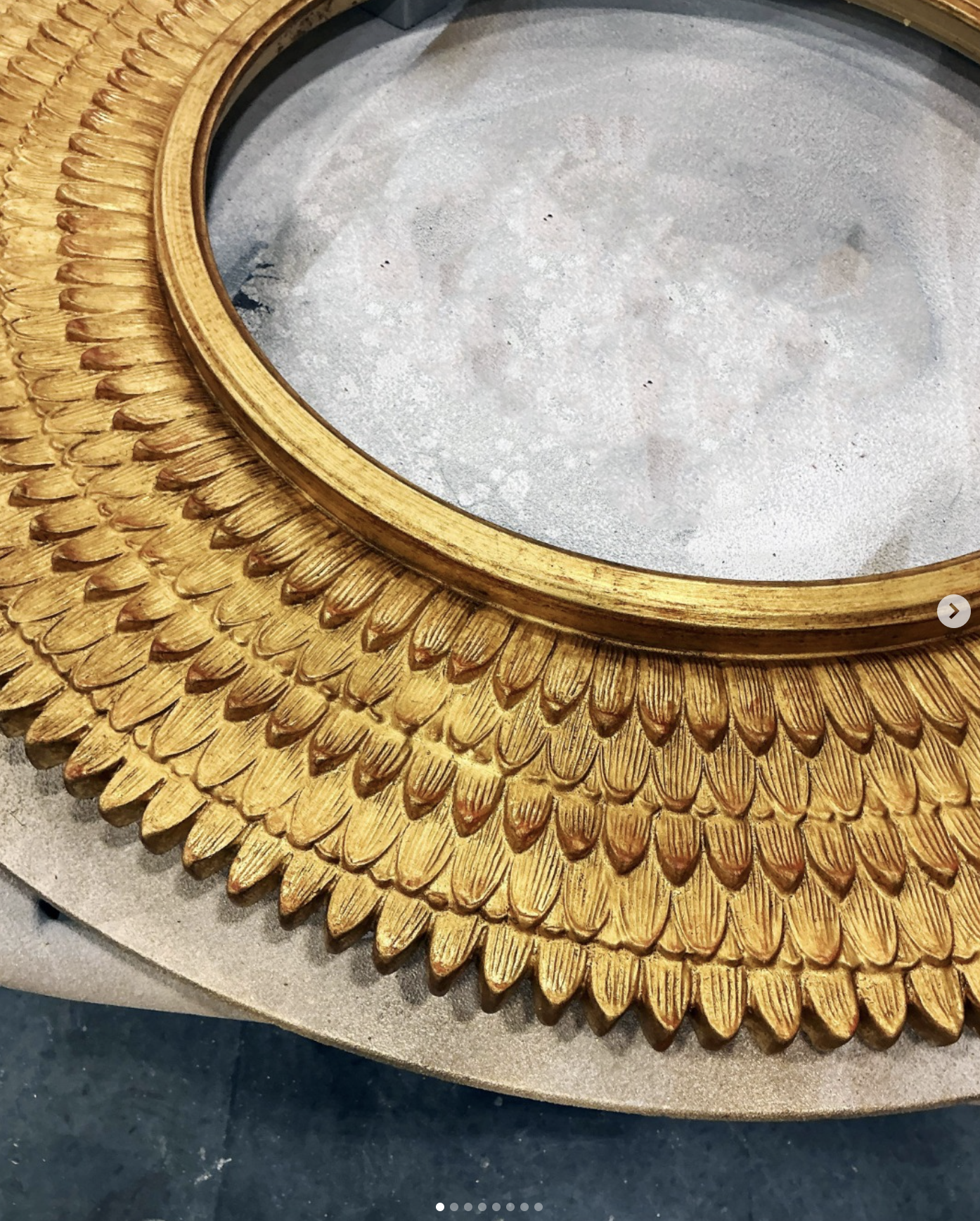 A decorative circular mirror with a gold frame that has a textured feather-like pattern around the edge.