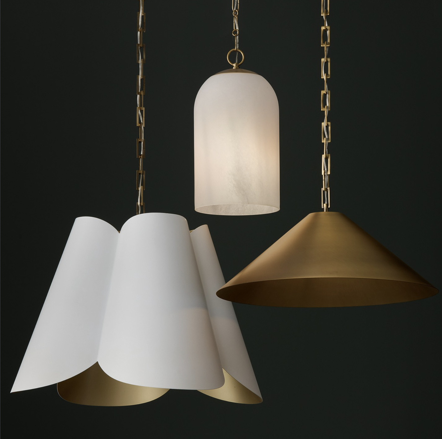 Close-up of three hanging pendant lights with different shades: white, white with a scalloped edge, and metallic gold, against a dark background.