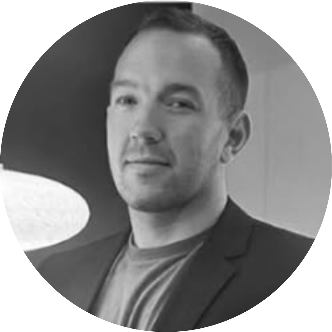 Black and white portrait of a man with short hair, wearing a blazer over a T-shirt, looking at the camera.