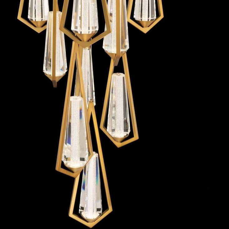 Close-up of a modern chandelier with multiple crystal pendants encased in gold geometric frames against a black background.