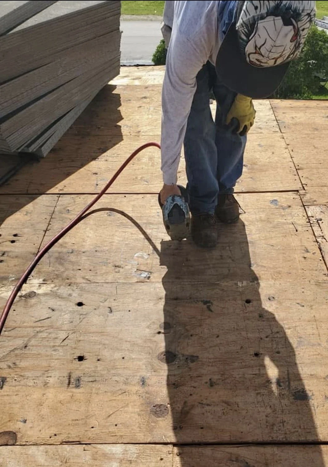 A worker on a wooden construction site using a power drill, wearing a cap, gloves, and protective clothing.