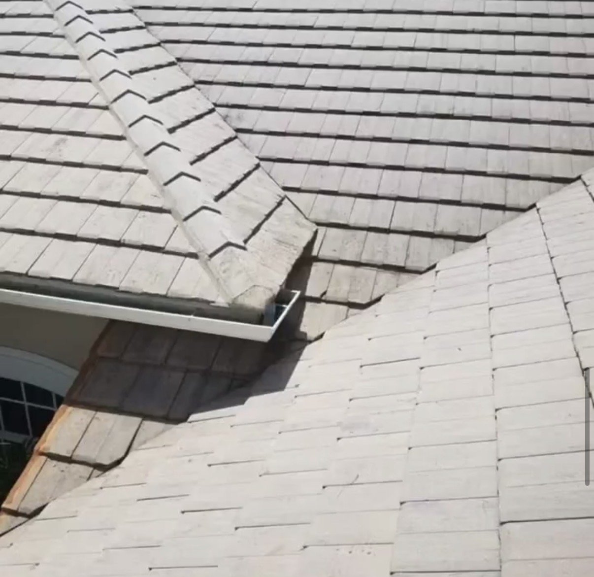 Close-up view of a multi-section roof with tan-colored shingles, including a gable and valley roofing areas, with a visible metal gutter.
