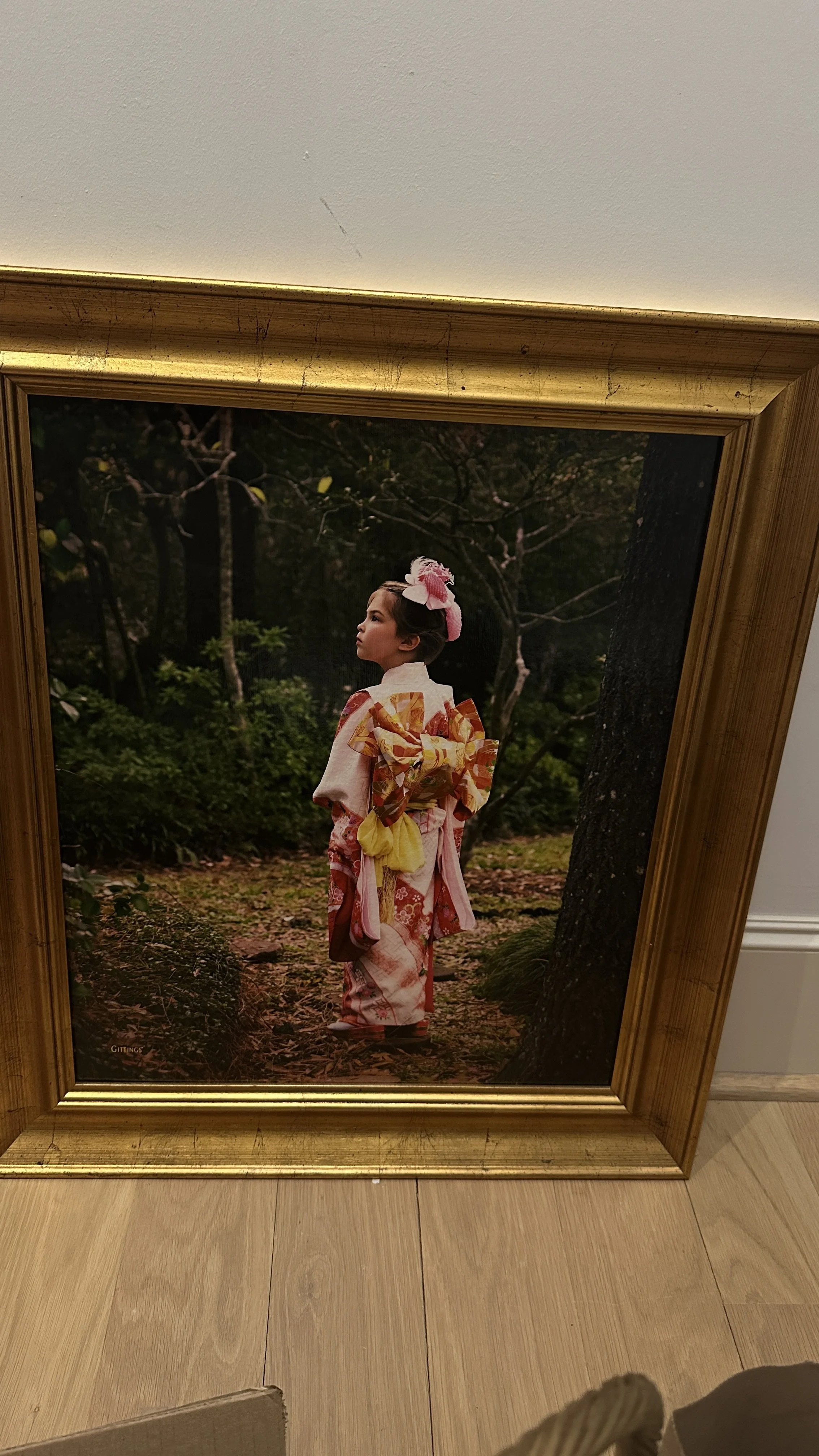 A framed photograph of a young girl in a kimono standing outdoors near trees and greenery.