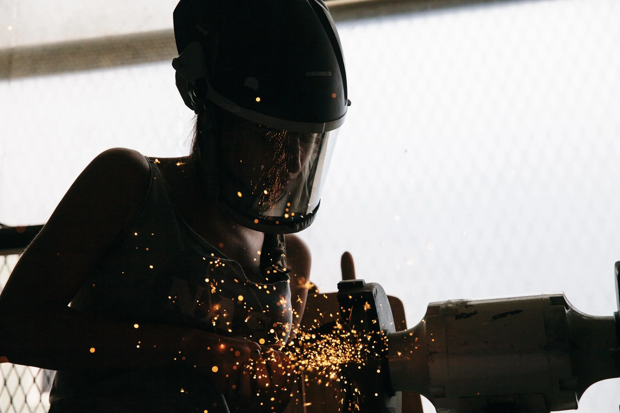 A person wearing a welding helmet is welding, creating bright sparks in a dark environment.